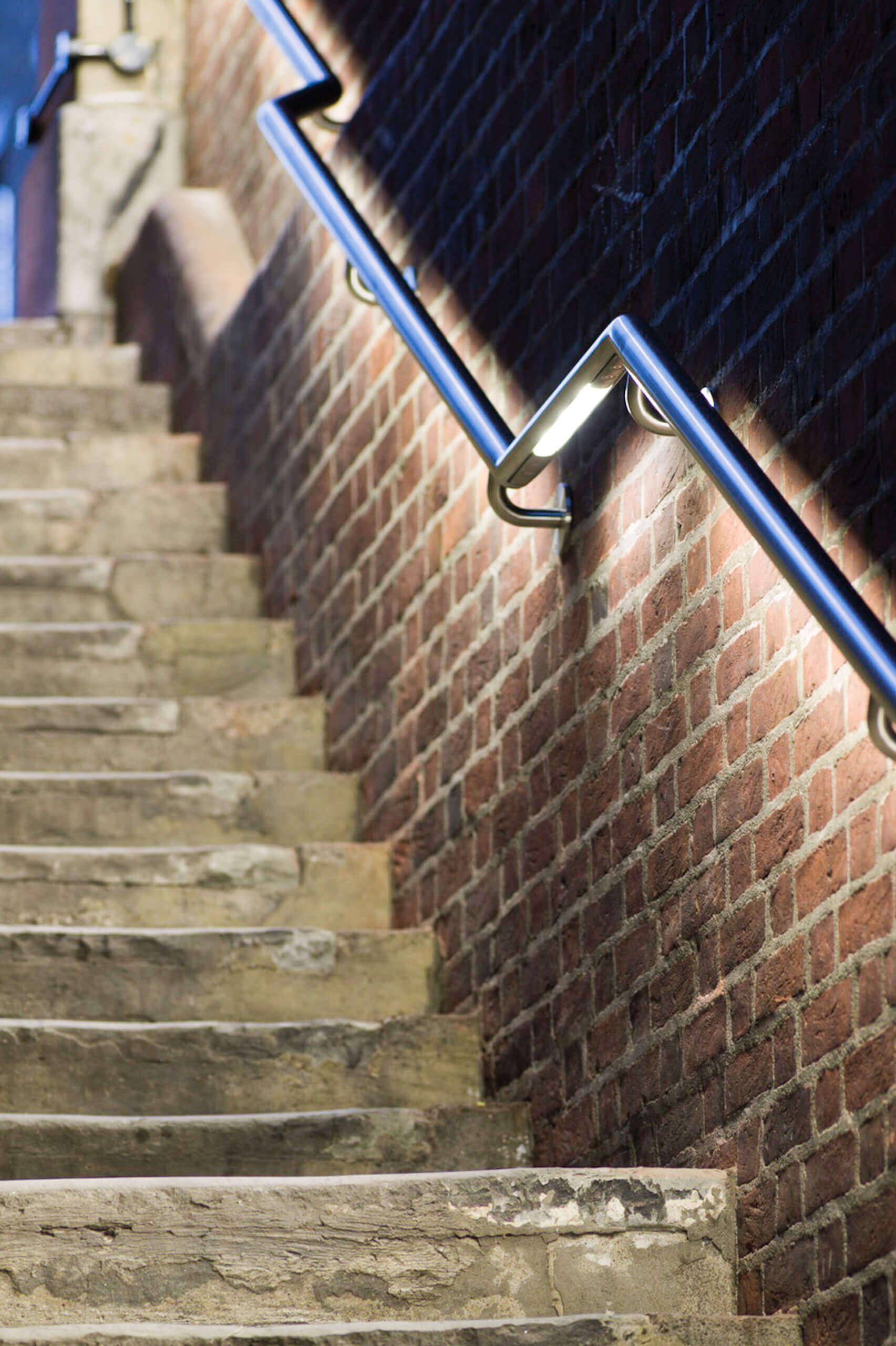 Beleuchtete Steintreppe mit Ziegelmauer und Edelstahlgeländer – Stadtmobiliar