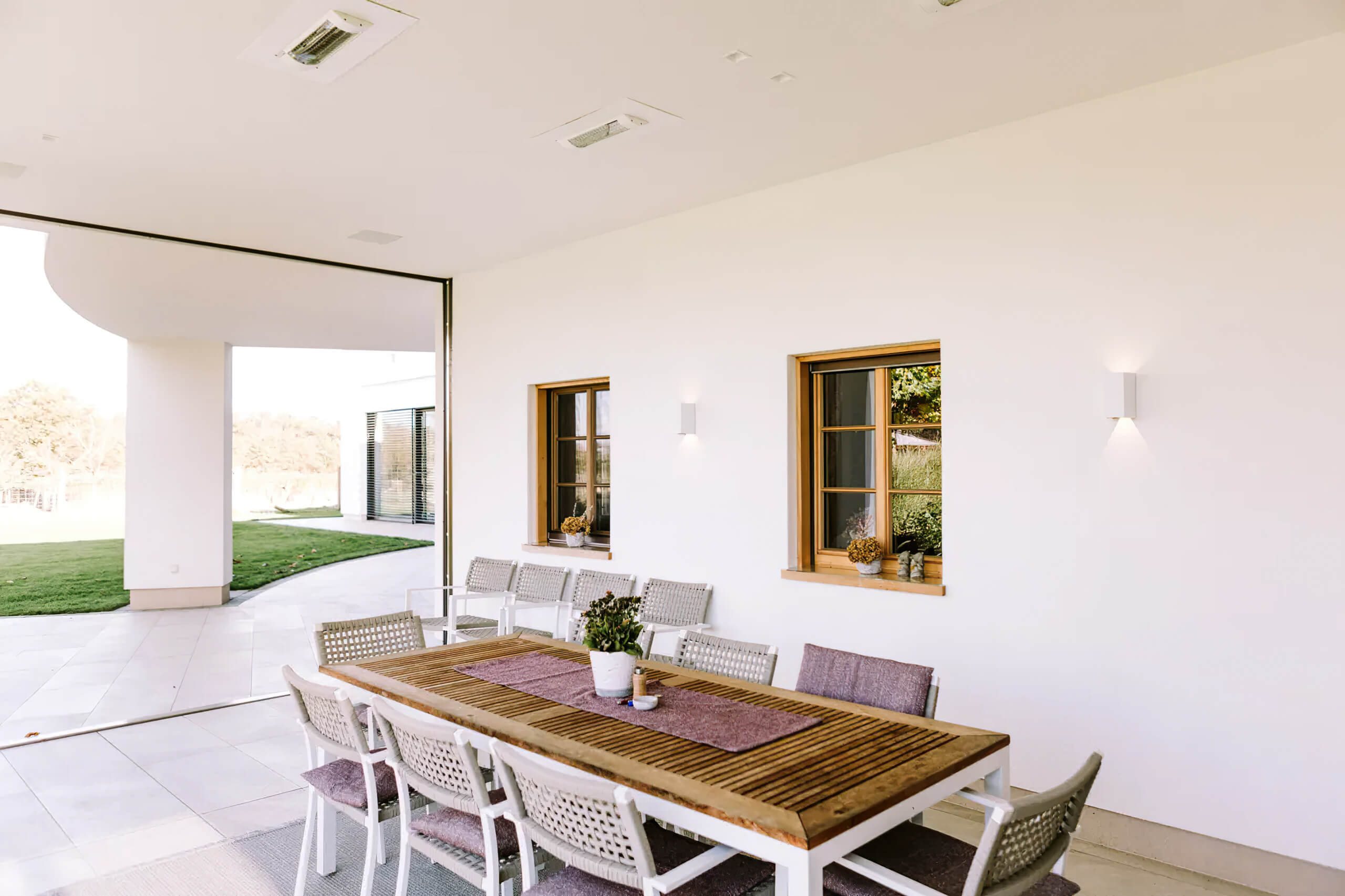 Überdachte Terrasse mit Esstisch und Stühlen, beleuchtet durch Wandleuchten