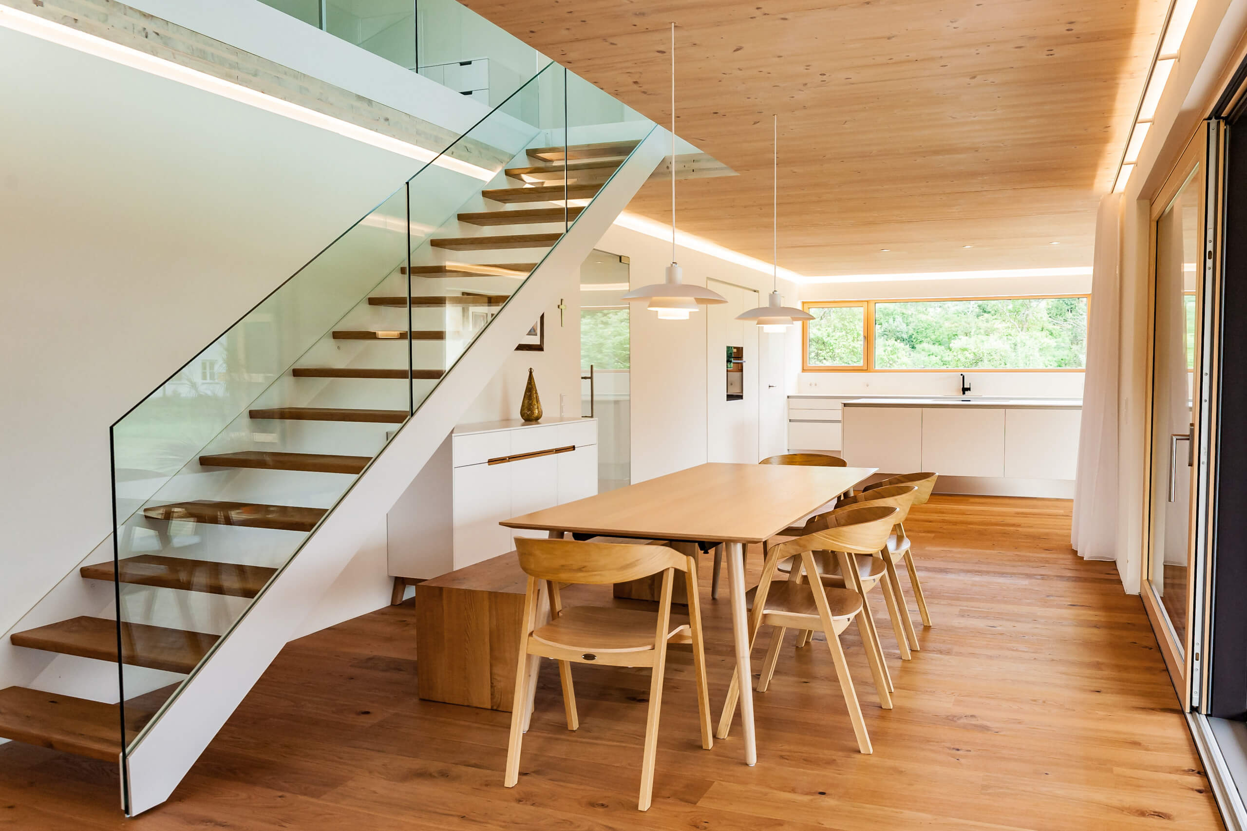Moderne Holztreppe mit Glasgeländer und Essbereich – Lichtplanung für Privat.