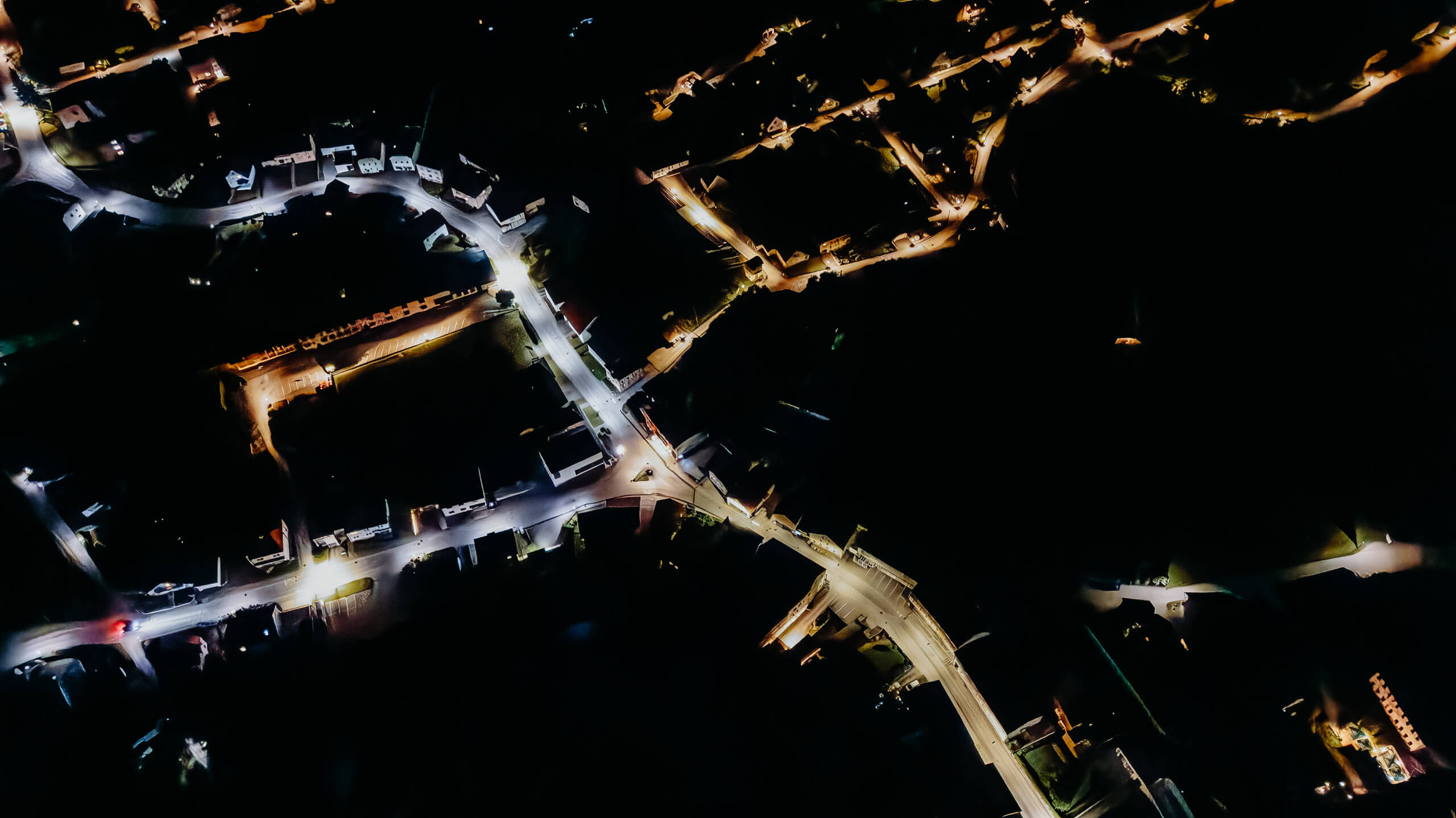 Luftaufnahme einer beleuchteten Ortschaft bei Nacht, Straßenbeleuchtung illuminiert die Wege.