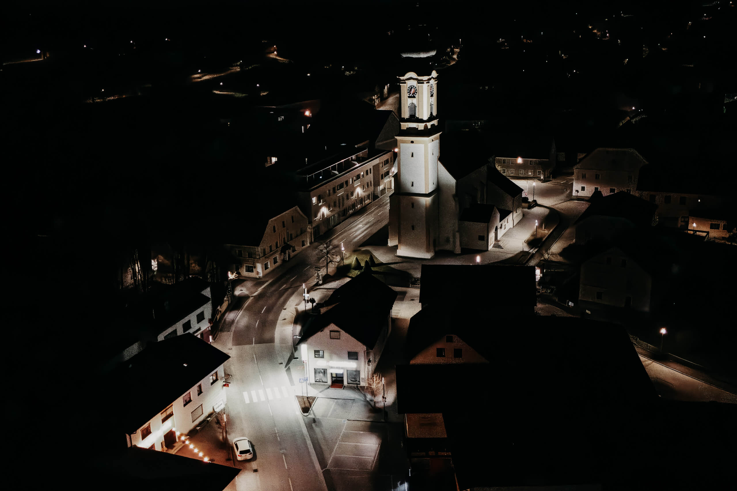 Ortsplatzgestaltung mit Kirchturm und Straßenbeleuchtung bei Nacht