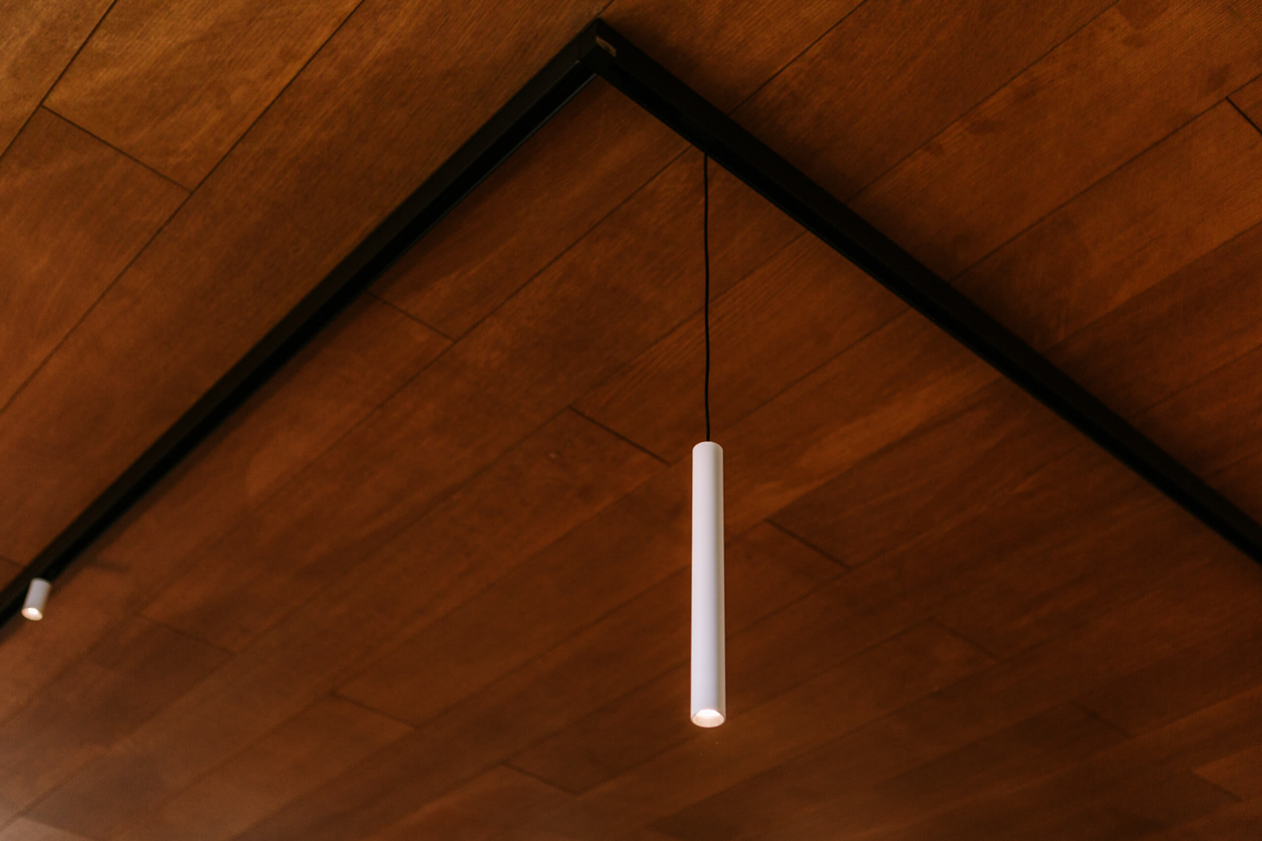 Moderne Deckenbeleuchtung mit zylindrischen Pendelleuchten auf Holzdecke.