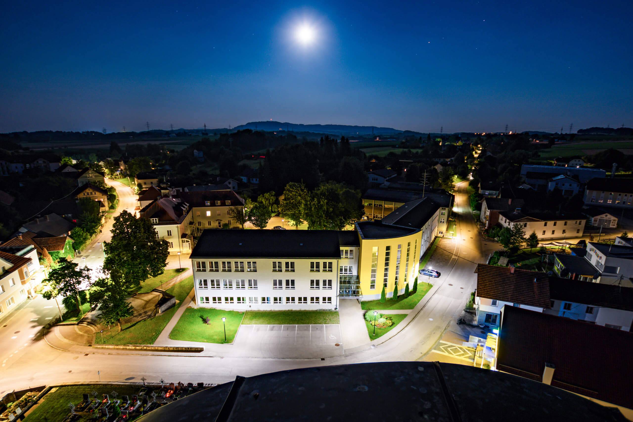 Beleuchtete Schule bei Nacht mit Mondlicht und Straßenlaternen
