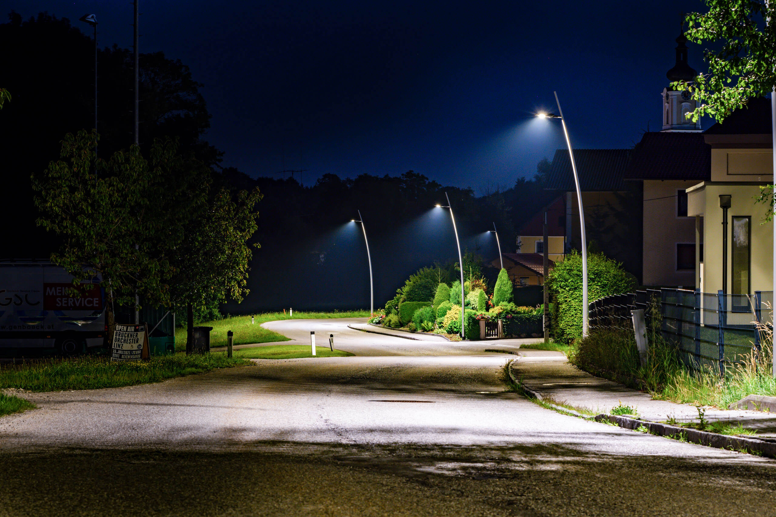 Beleuchtete Straße mit modernen Laternen und gepflegten Grünflächen bei Nacht