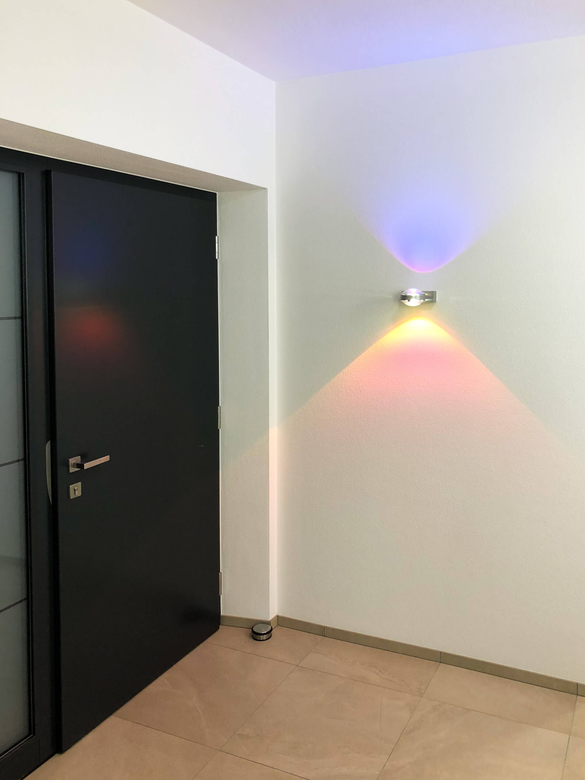 Moderne Innenbeleuchtung mit farbigen Lichtakzenten an einer Wand neben schwarzer Tür.