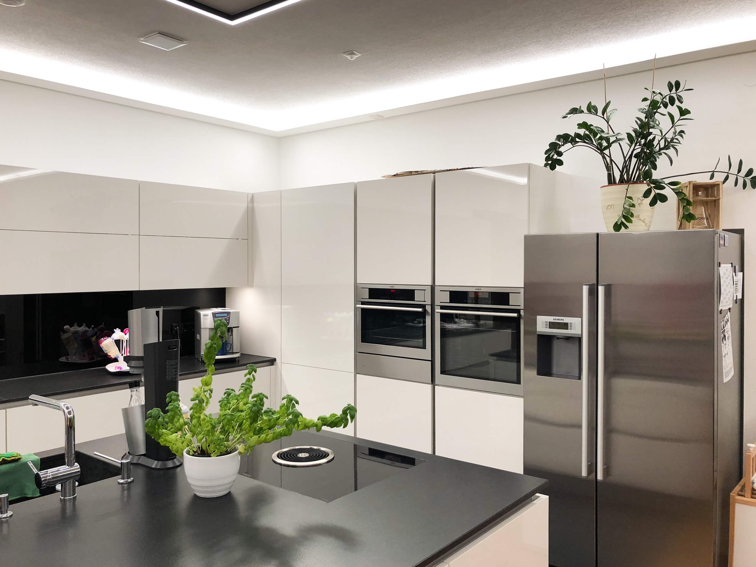 Moderne Küche mit Edelstahlgeräten, weißen Hochglanzfronten und integrierter Beleuchtung.