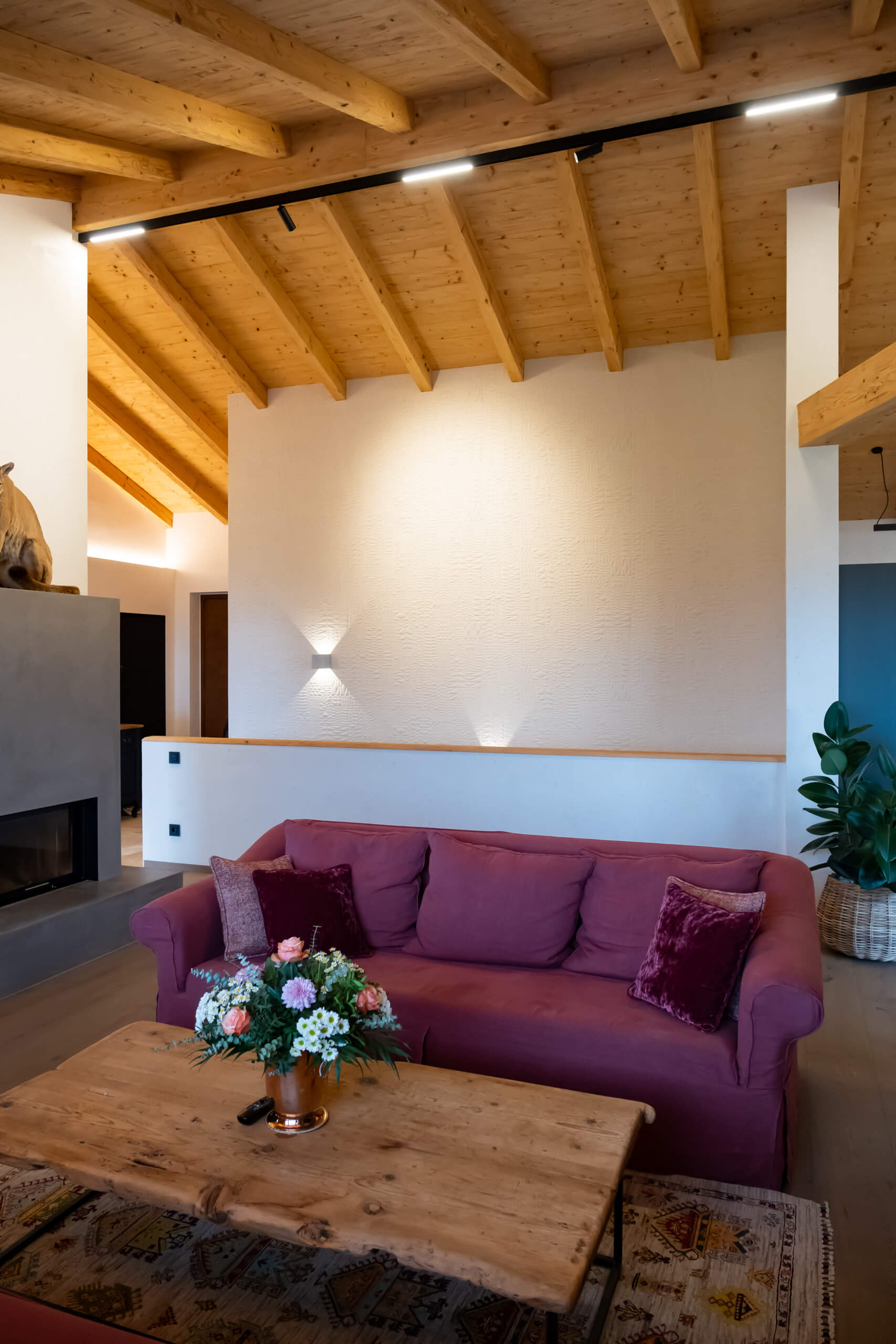 Modernes Wohnzimmer mit purpurrotem Sofa, Holzbalkendecke und Kamin – Lichtplanung von Illumina.