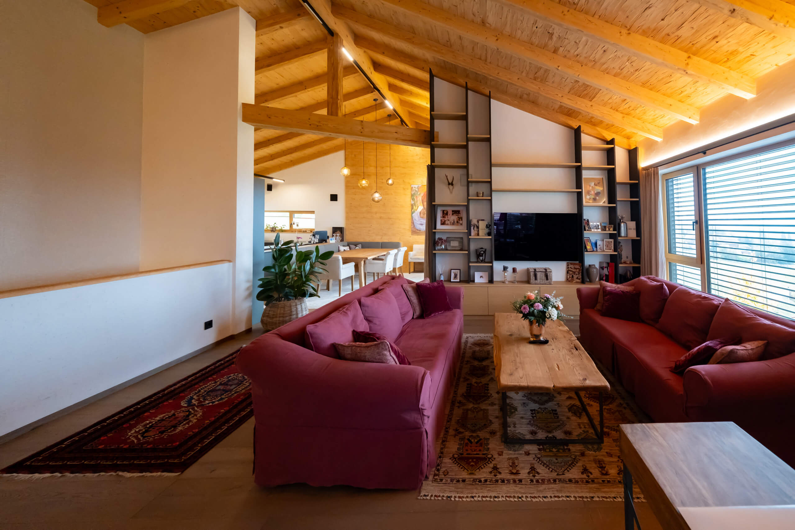 Modernes Wohnzimmer mit roten Sofas, Holzbalkendecke und indirekter Beleuchtung.