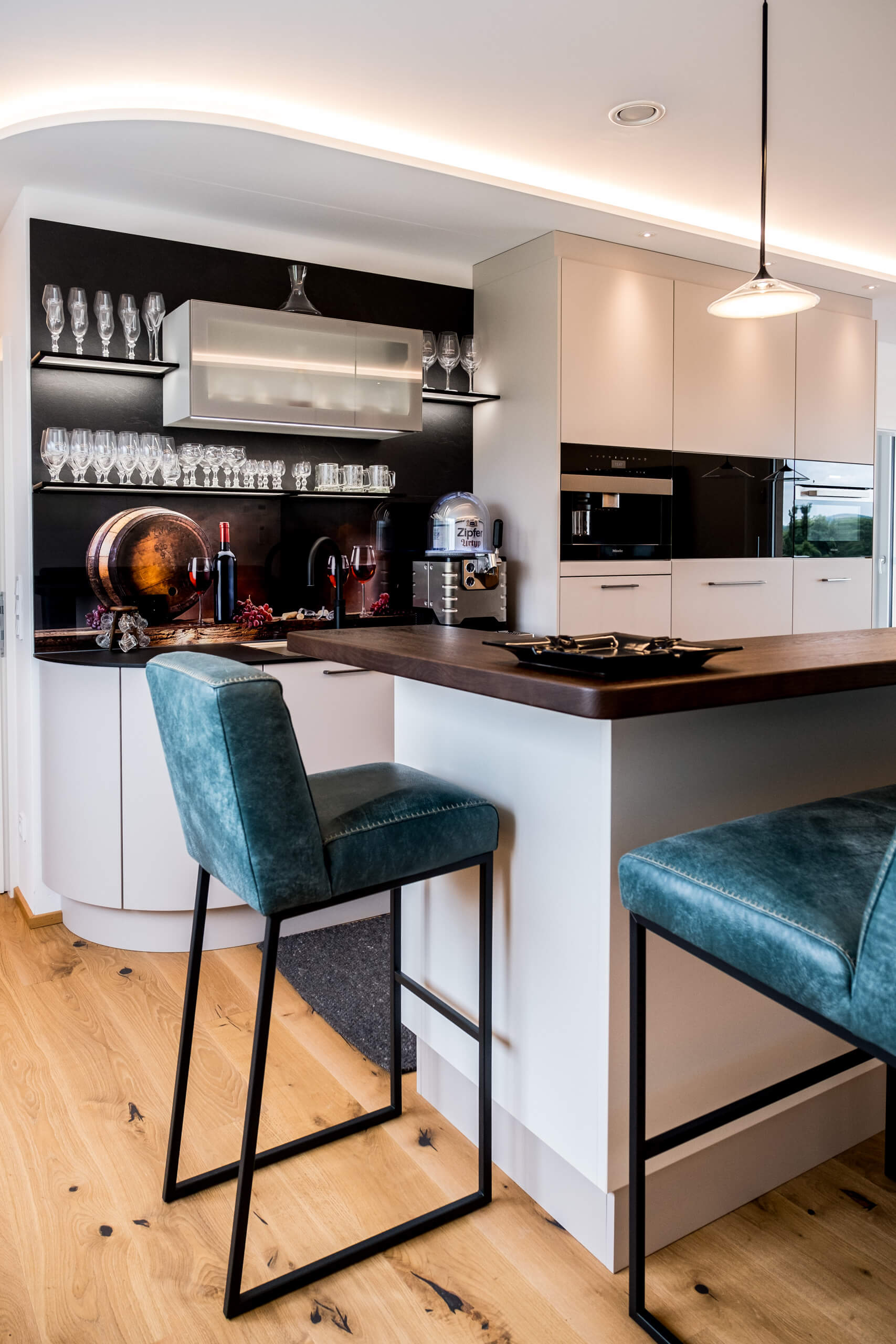 Moderne Küche mit Bar und Sitzhockern, beleuchtet durch indirektes Licht.
