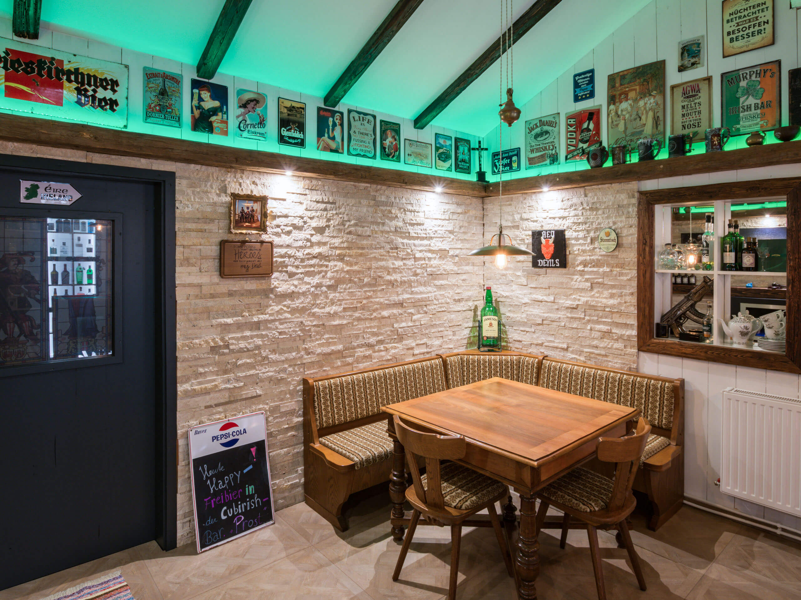 Gemütlicher Barbereich mit Holztischen und Sitzbänken, beleuchtet von grüner Deckenbeleuchtung.