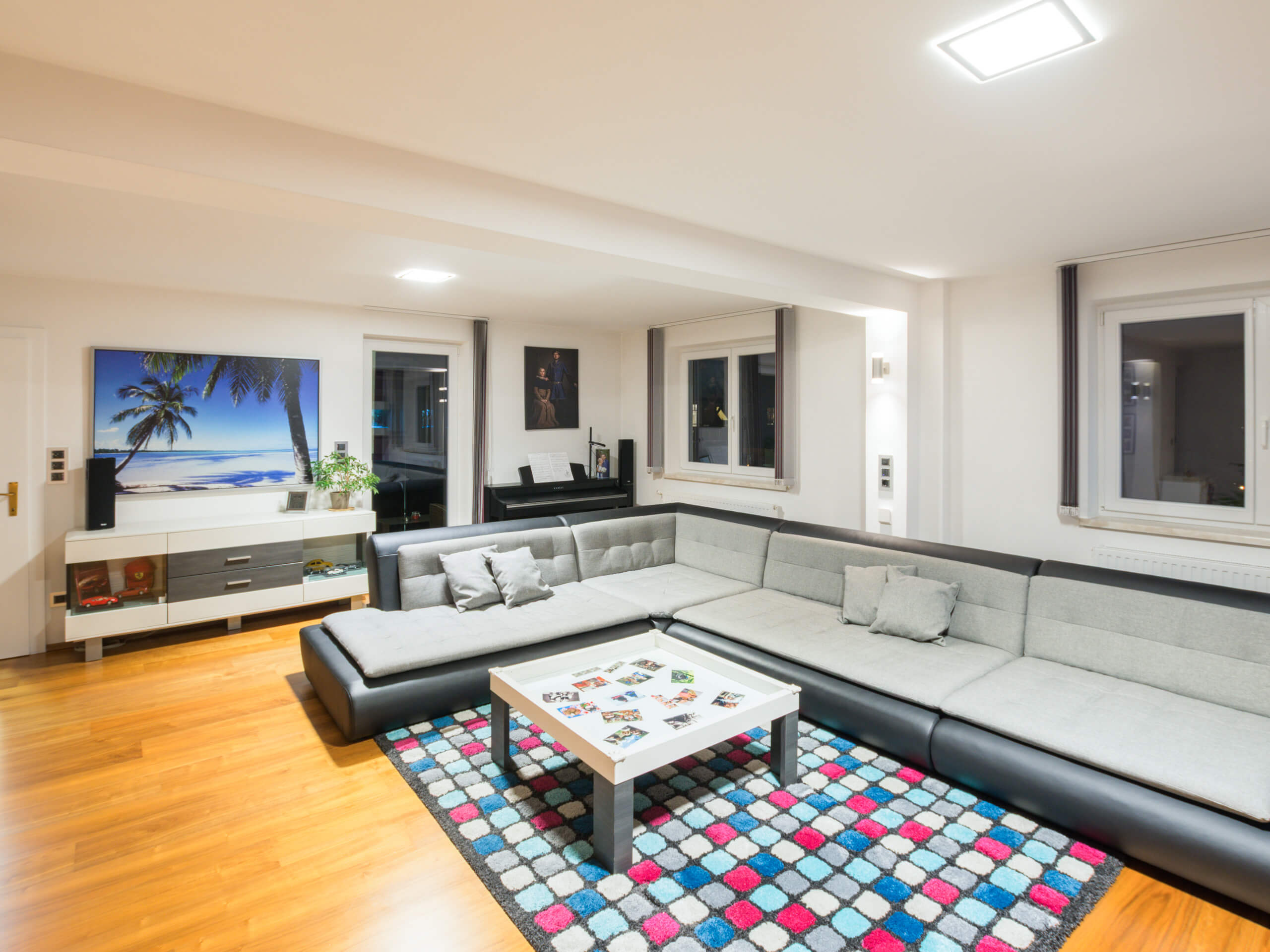 Modernes Wohnzimmer mit großem Sofa, Teppich und beleuchtetem Deckenlicht.
