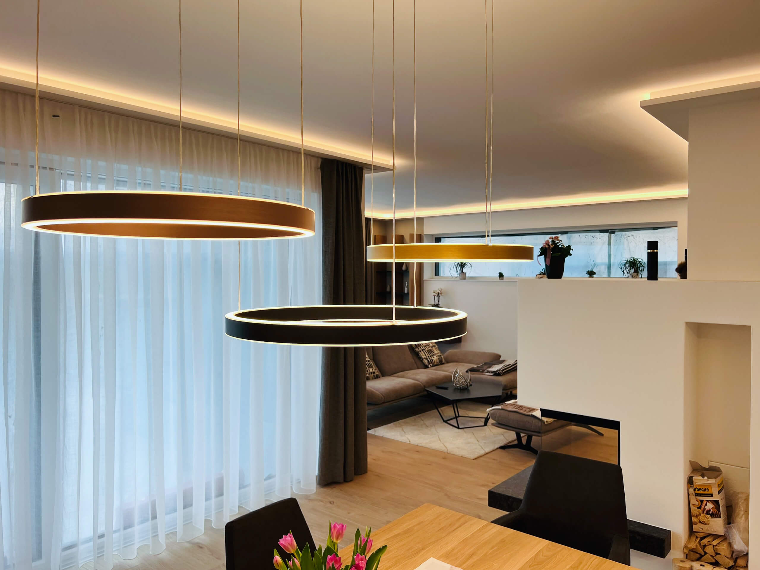 Modernes Wohnzimmer mit Ring-Hängeleuchten, Kamin und gemütlicher Sitzecke – Lichtplanung von Illumina.