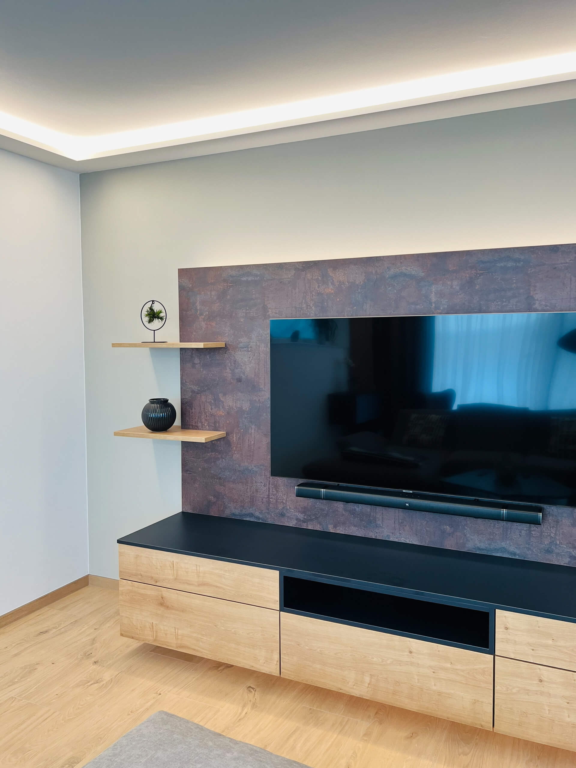 Modernes Wohnzimmer mit großem Flachbildfernseher, dunkler Soundbar und Holzböden.