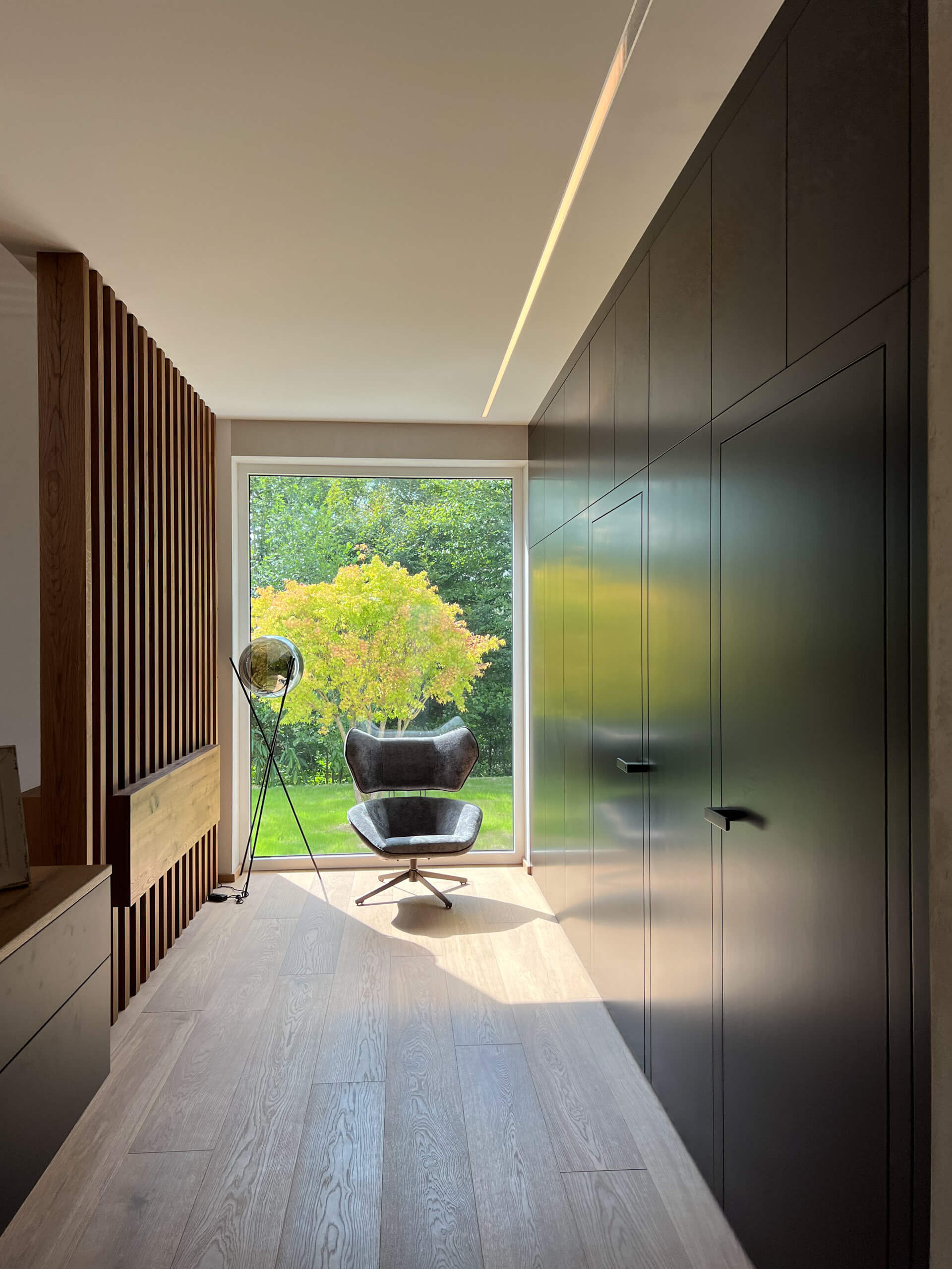 Modernes Interieur mit einem Sessel vor einem Fenster, beleuchtet durch eine Deckenleiste und eine Stehleuchte.