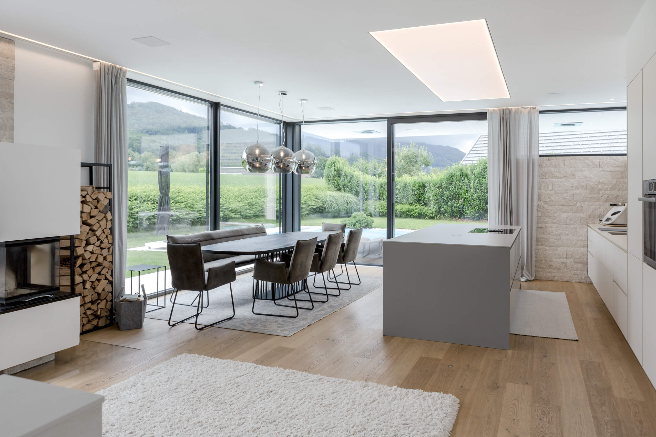 Moderne Wohnküche mit Essbereich und Kamin, beleuchtet durch elegante Hängeleuchten von Illumina.
