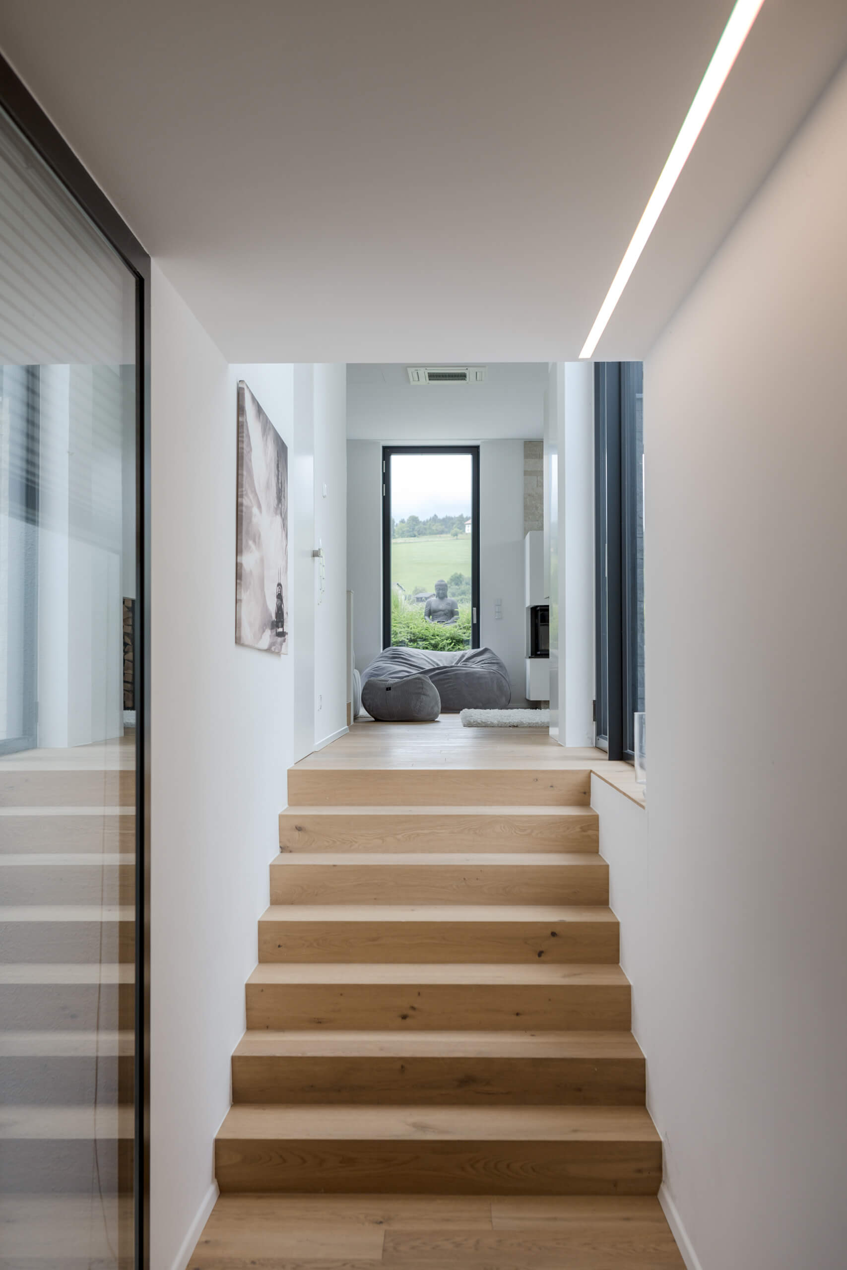 Moderne Holztreppe führt zu einem hellen Wohnbereich mit Sitzsäcken und Fenster.