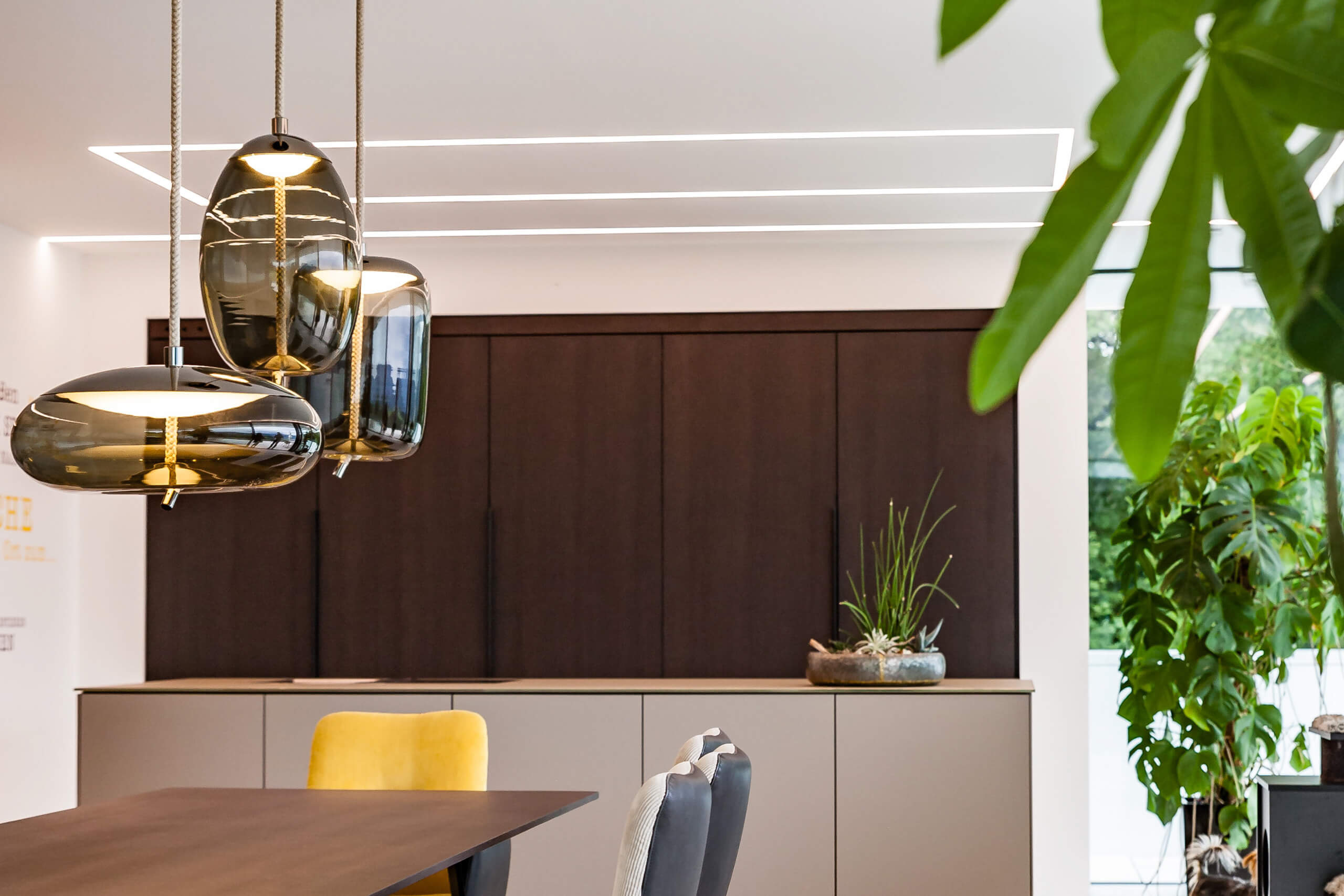 Moderne Küche mit dunklen Holzfronten, Essbereich und indirekter Beleuchtung – Lichtplanung von Illumina.