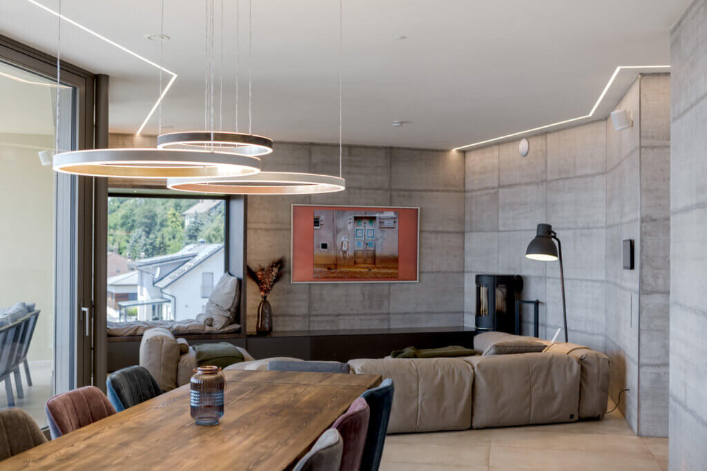 Modernes Wohnzimmer mit Betonwänden, Kamin, Ecksofa und Hängeleuchten – Lichtplanung von Illumina.