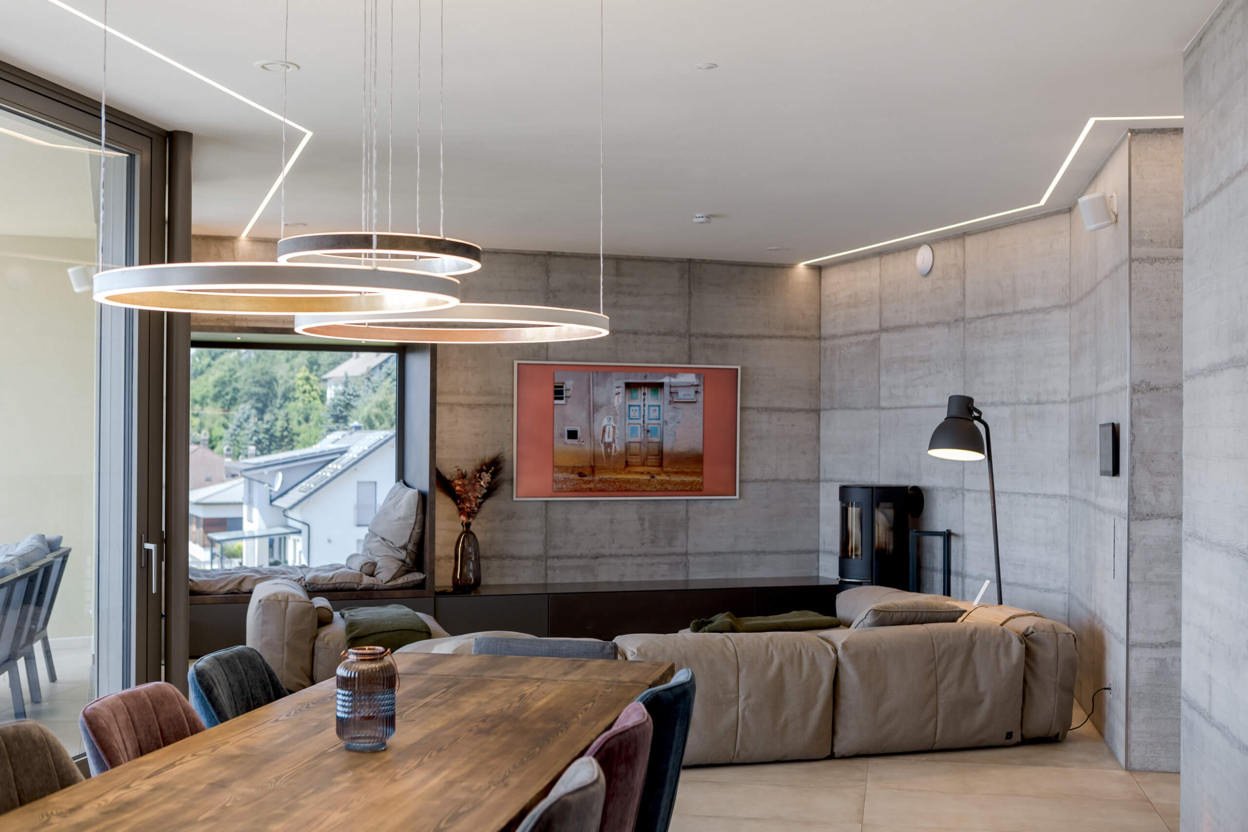 Modernes Wohnzimmer mit Betonwänden, Kamin, Ecksofa und Hängeleuchten – Lichtplanung von Illumina.
