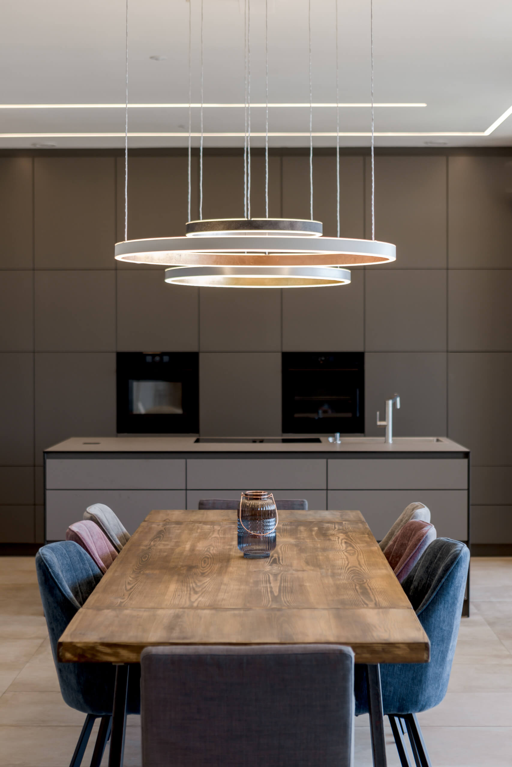 Moderne Esszimmerbeleuchtung mit Hängeleuchten über Holztisch und Stühlen.