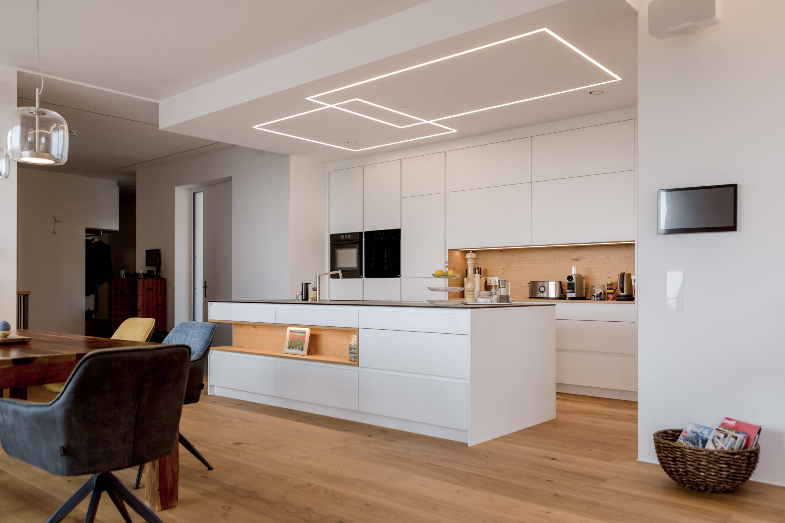 Moderne weiße Küche mit Kochinsel und integrierten Leuchten, beleuchtet von Illumina.