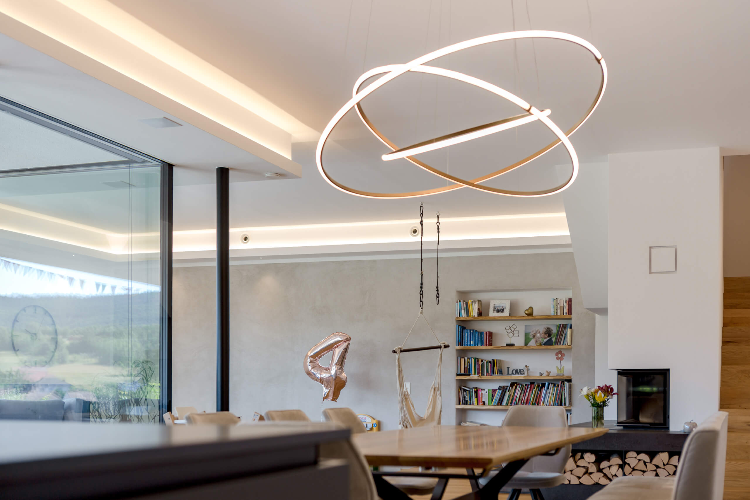 Modernes Wohnzimmer mit Hängeleuchte, Kamin und Bücherregal – Lichtplanung von Illumina.