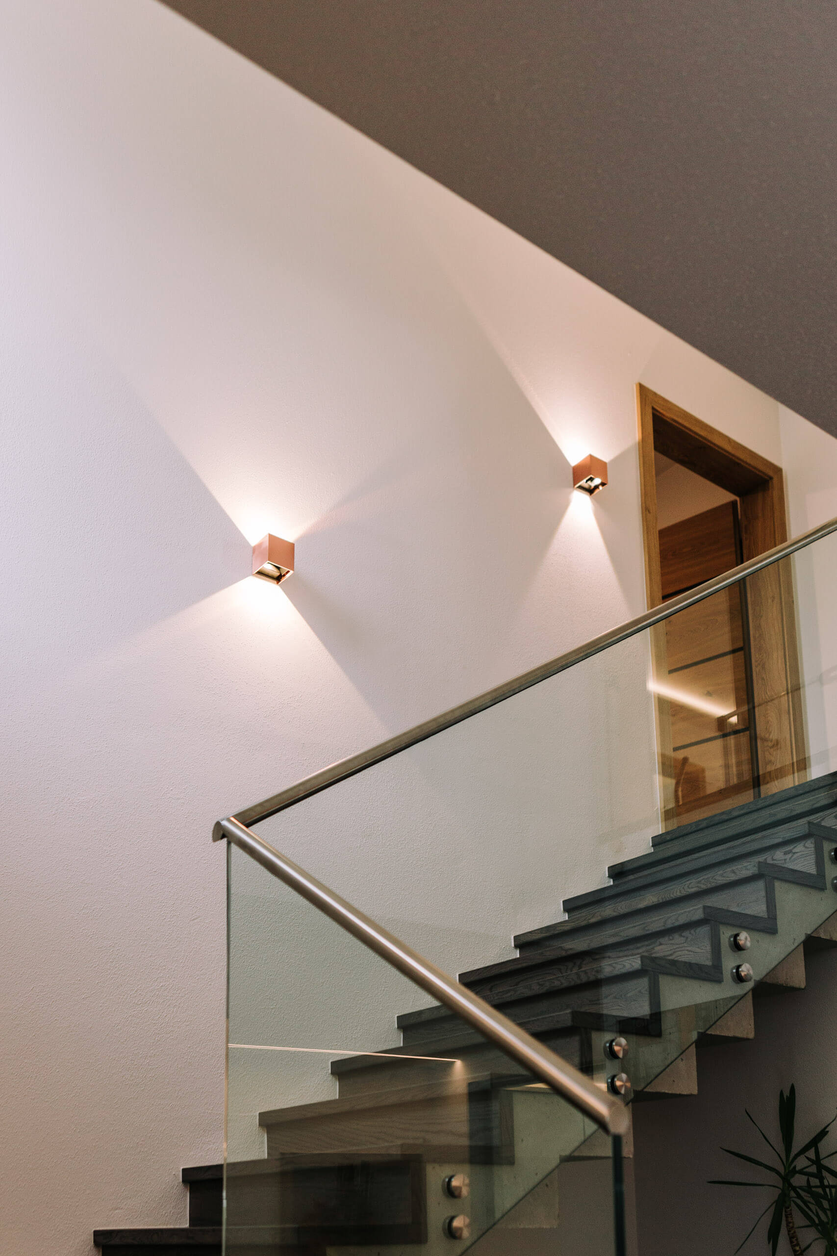 Beleuchtete moderne Treppe mit Glasgeländer und Wandleuchten.