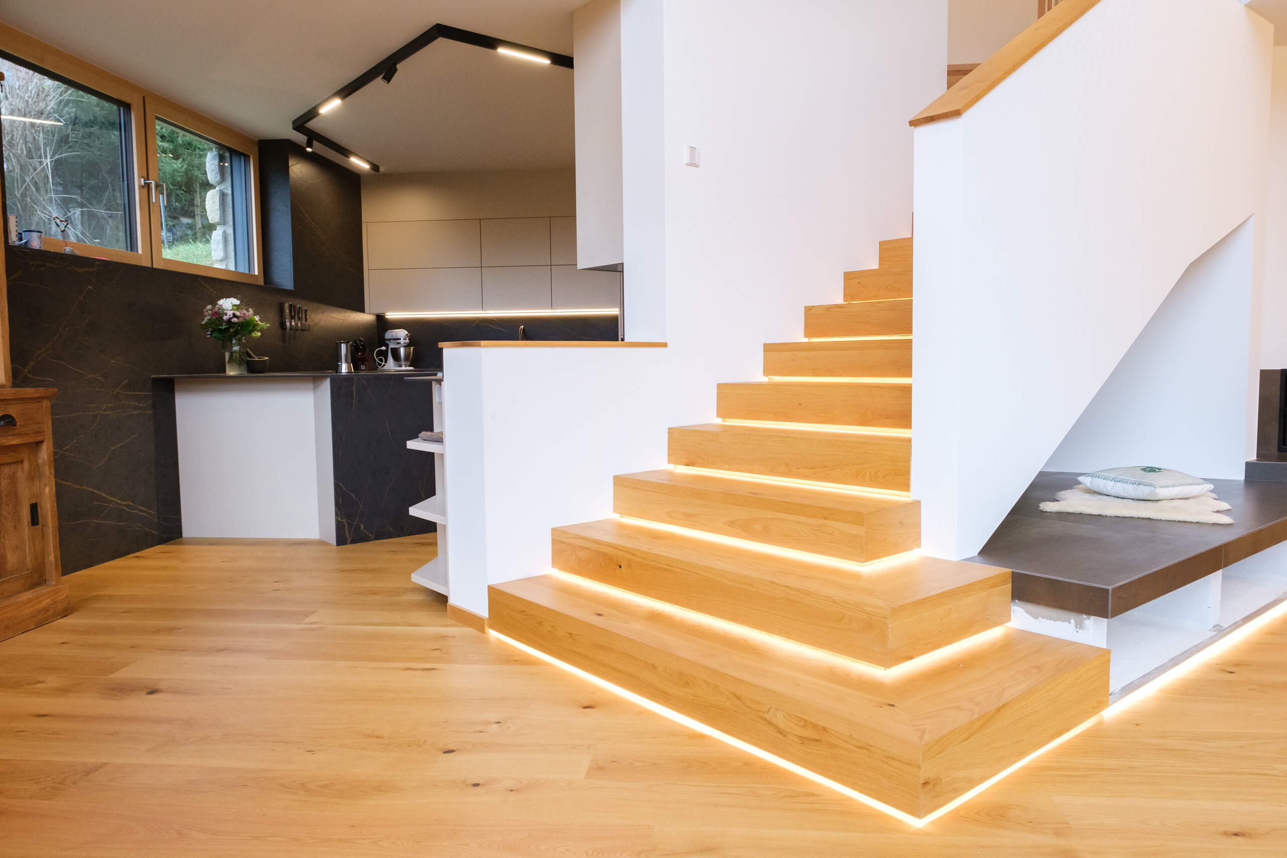 Moderne Holztreppe mit indirekter Beleuchtung und angrenzendem Küchenbereich