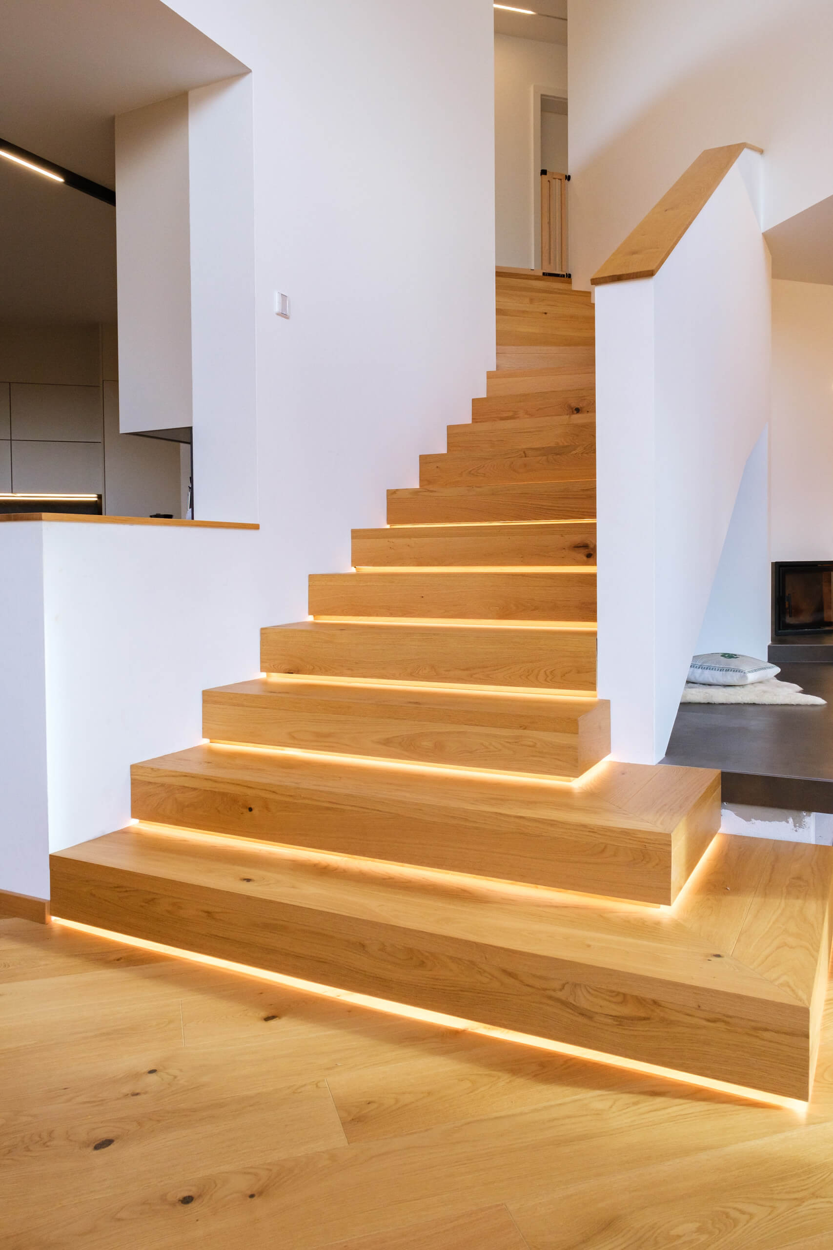 Moderne Holztreppe mit integrierter LED-Beleuchtung und weißer Wand – Lichtplanung von Illumina.