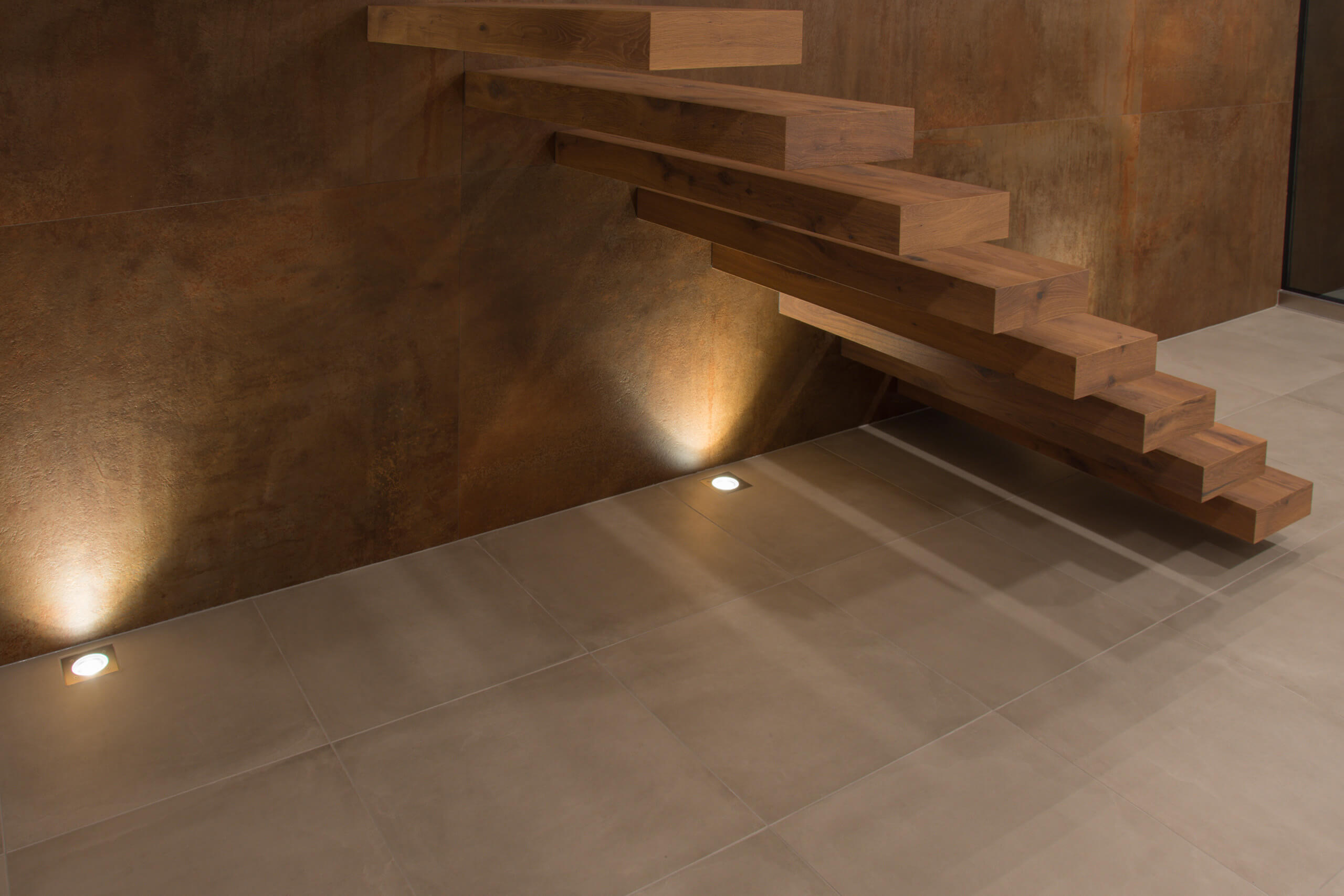 Moderne Holztreppe mit integrierter Beleuchtung vor brauner Wand – Lichtplanung von Illumina.