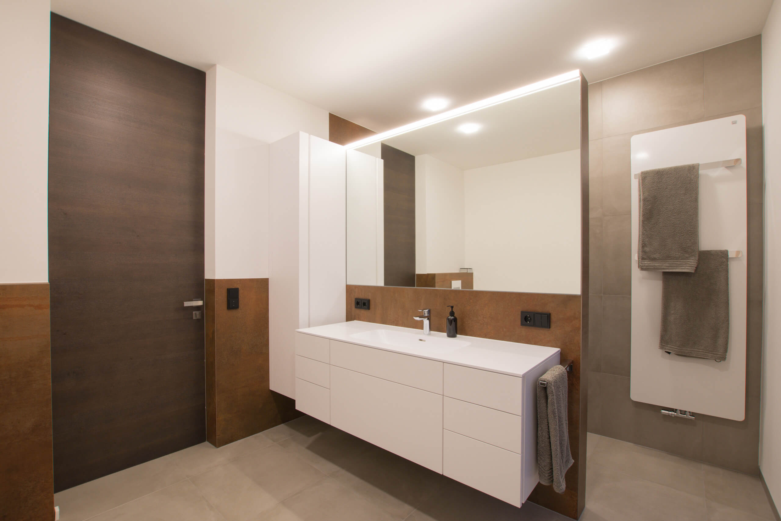 Modernes Badezimmer mit schwebendem Waschtisch, Spiegel und Handtuchwärmer – Lichtplanung von Illumina.