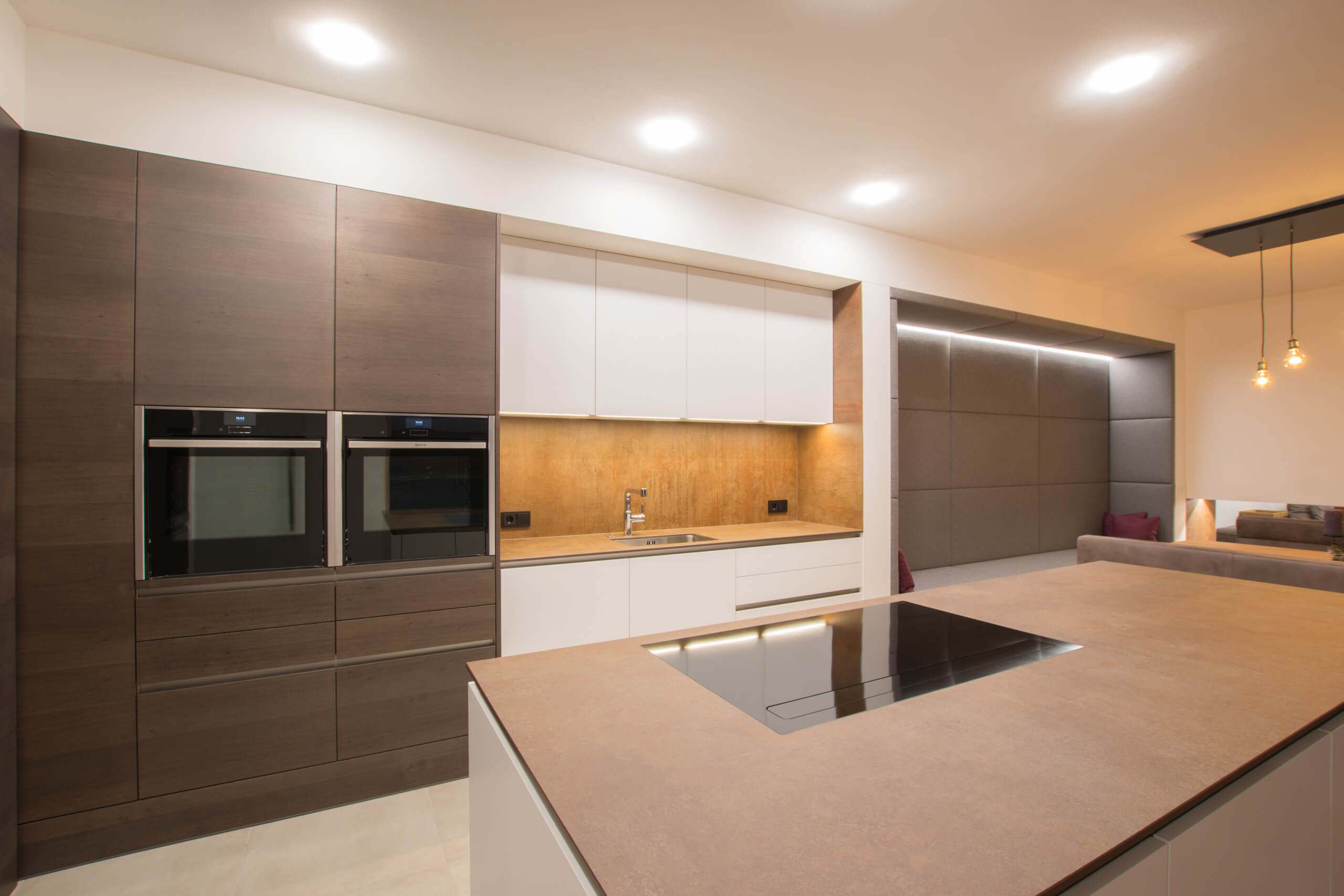 Moderne Küche mit dunklen Holzfronten, weißen Oberschränken und Kochinsel – Lichtplanung von Illumina.