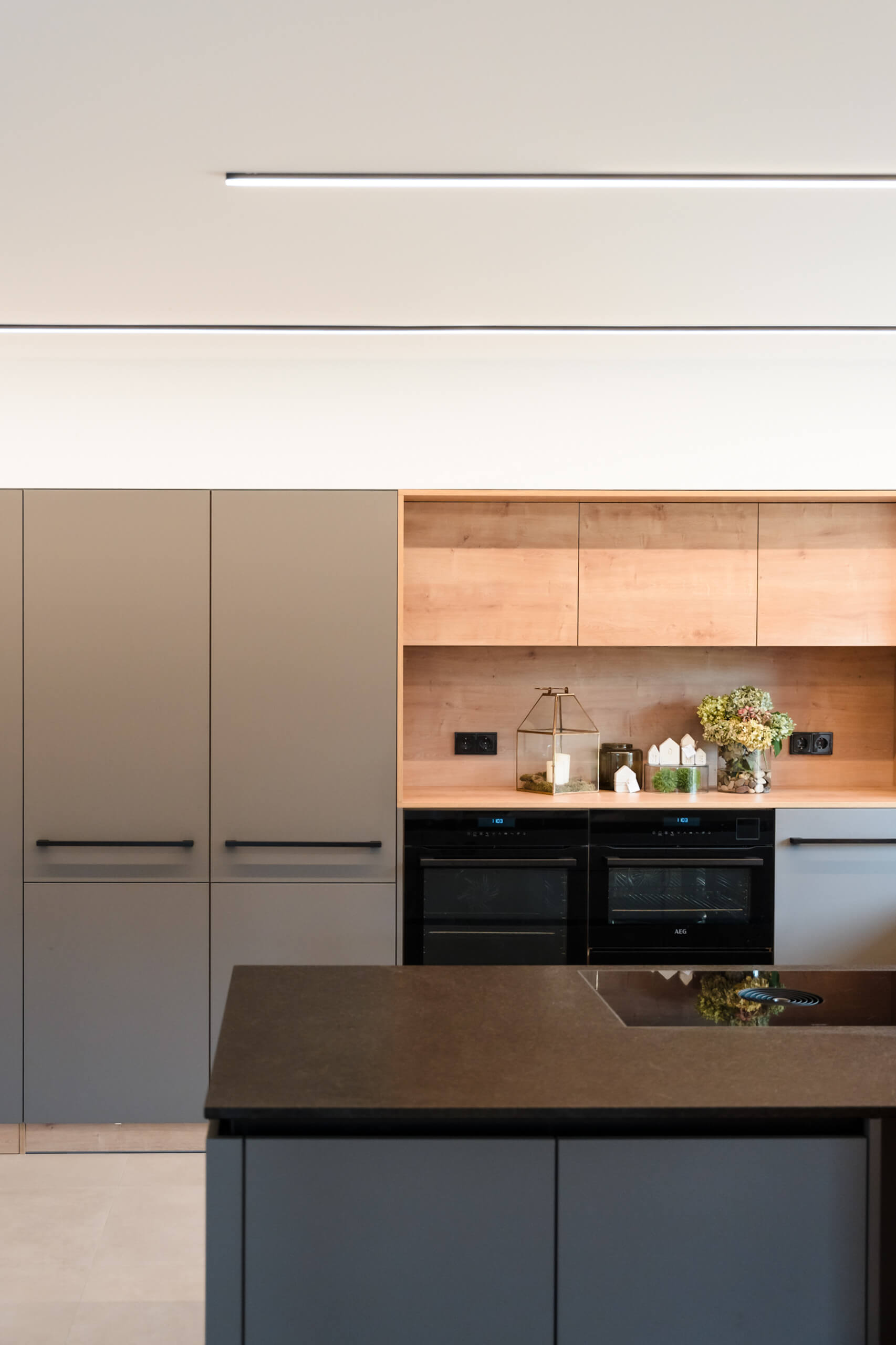 Moderne Küche mit integrierten Geräten und Holzakzenten, beleuchtet durch eine lineare Pendelleuchte.