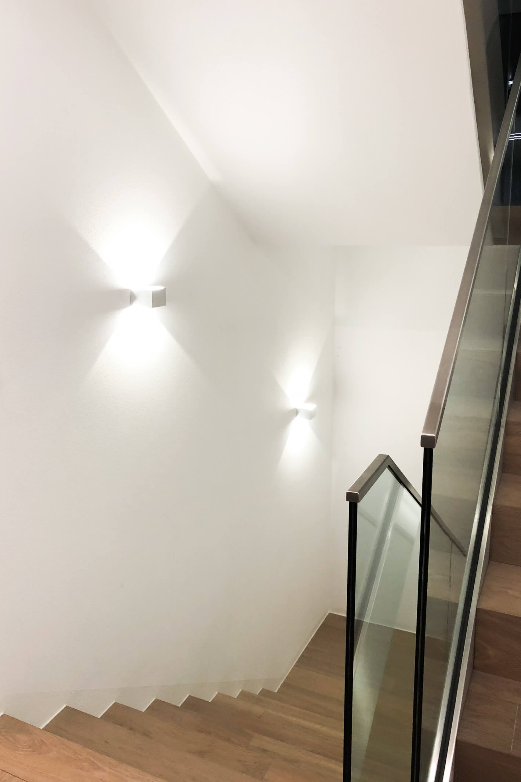 Moderne Treppe mit Glasgeländer und Wandleuchten – Lichtplanung von Illumina