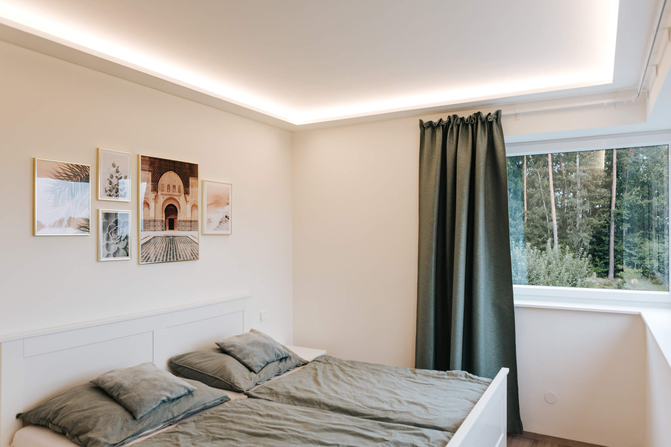 Modernes Schlafzimmer mit indirekter Deckenbeleuchtung und Blick ins Grüne