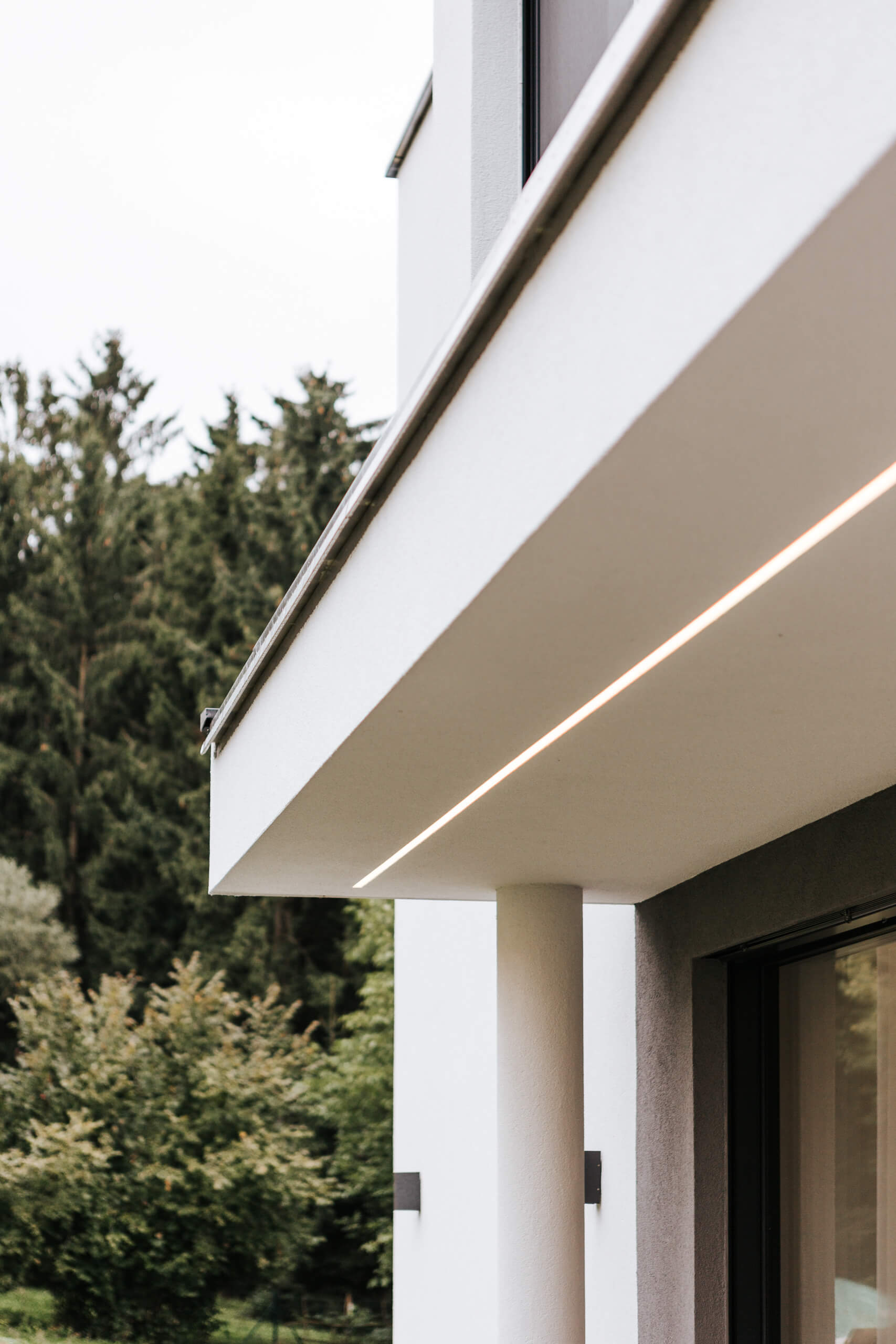 Moderne Architektur mit dezenter Außenbeleuchtung und Wald im Hintergrund.