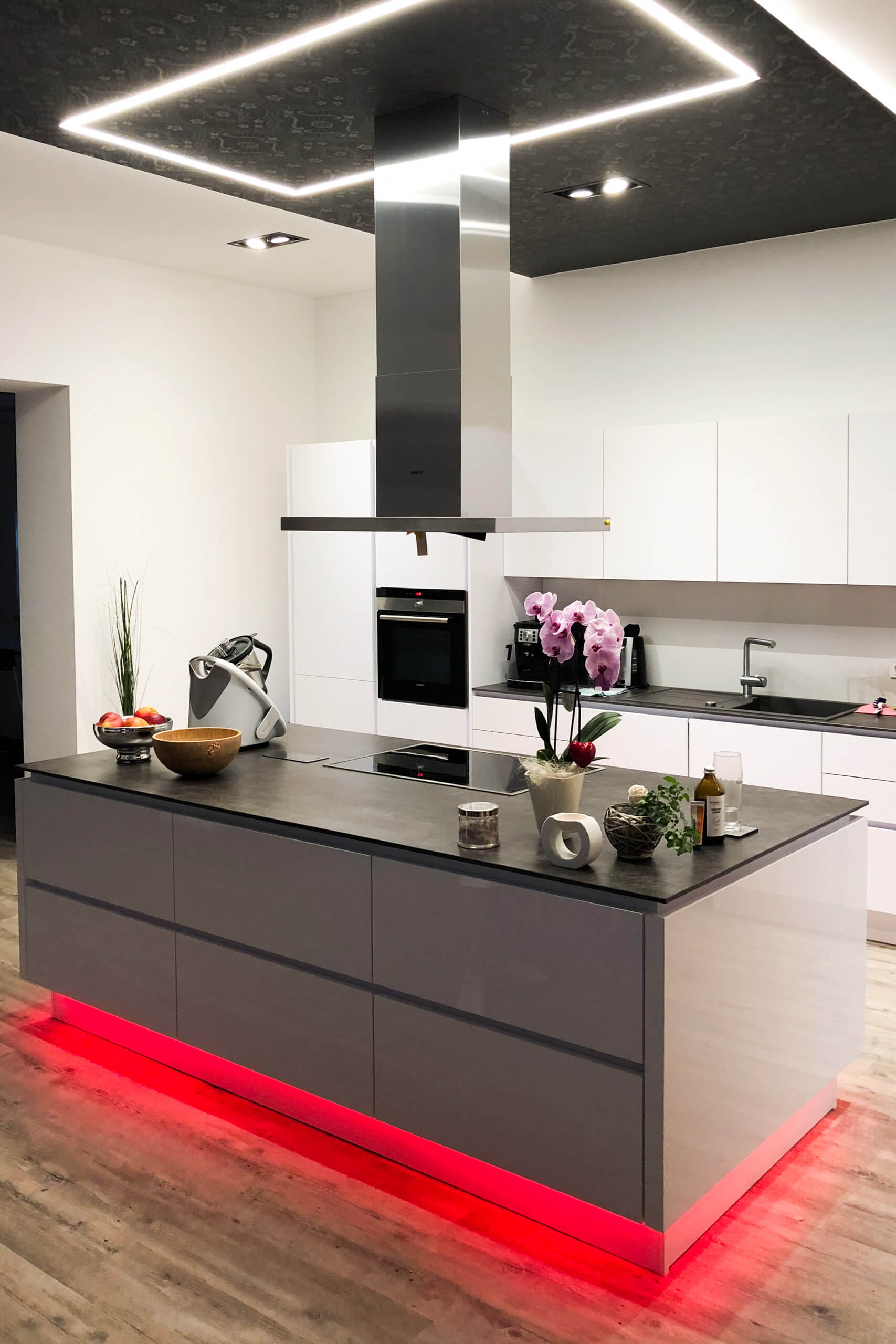 Moderne Küche mit Kochinsel, beleuchtet durch LED-Akzente und Deckenbeleuchtung.