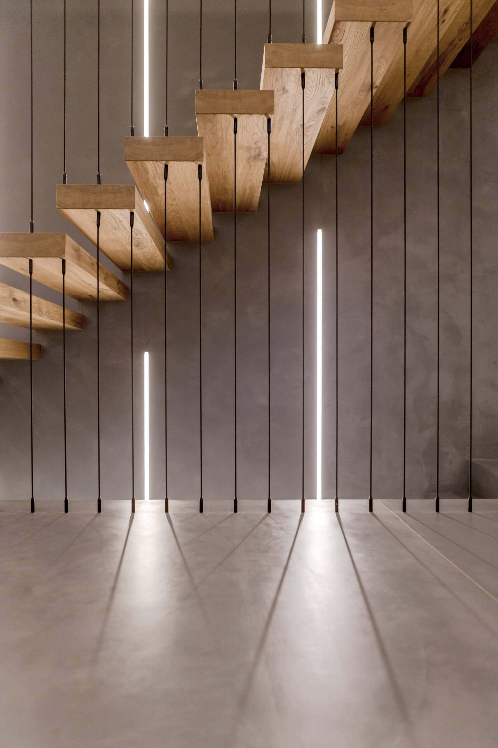 Moderne Holztreppe mit vertikalen LED-Leuchten und Betonwand – Lichtplanung von Illumina