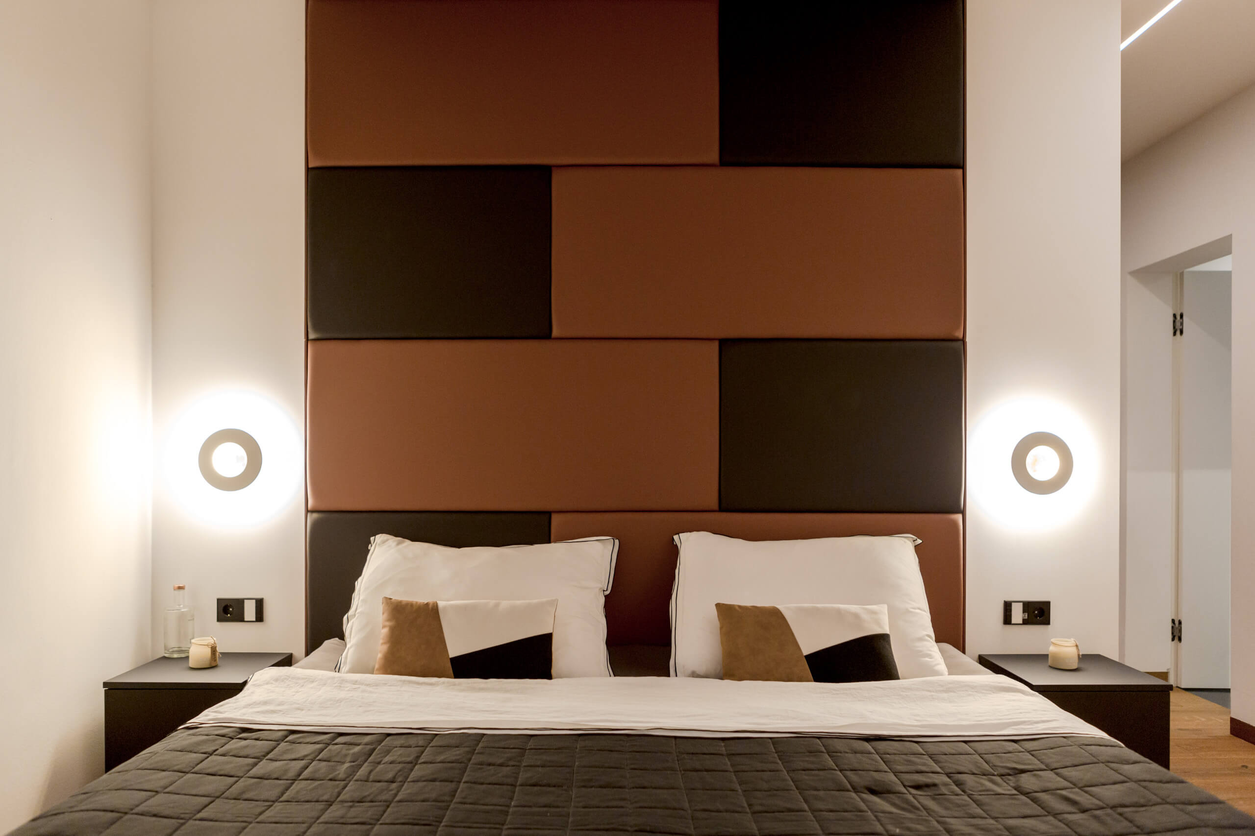 Modernes Schlafzimmer mit beleuchtetem Kopfteil und runden Wandleuchten