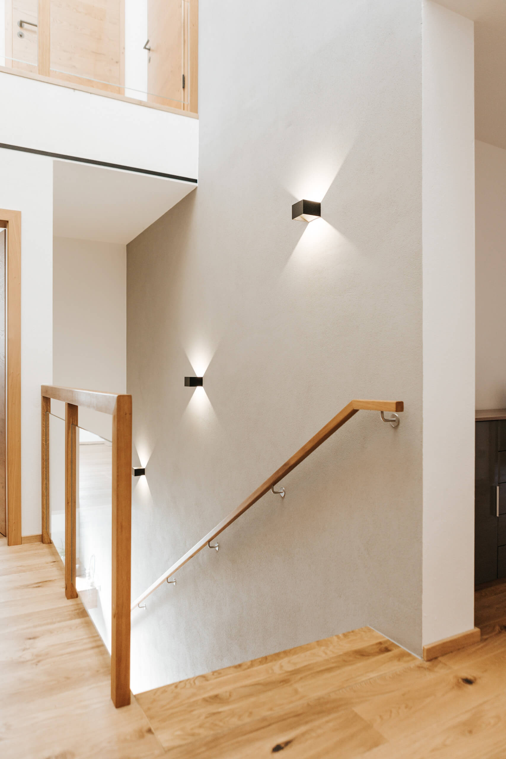 Moderne Treppe mit Holzhandlauf und indirekter Wandbeleuchtung