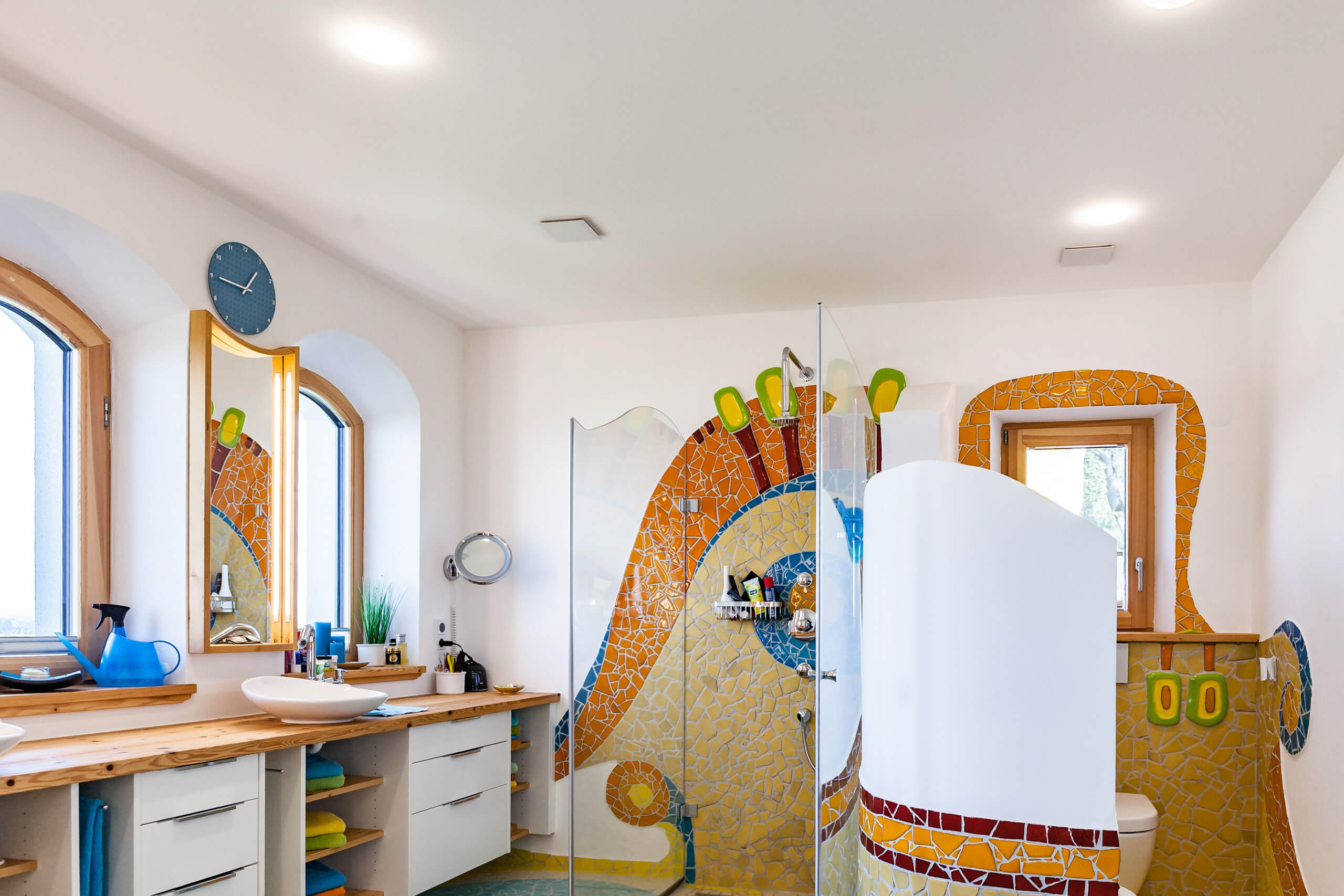 Badezimmer mit bunter Mosaikfliesen-Dusche, Waschbecken und Holzmöbeln
