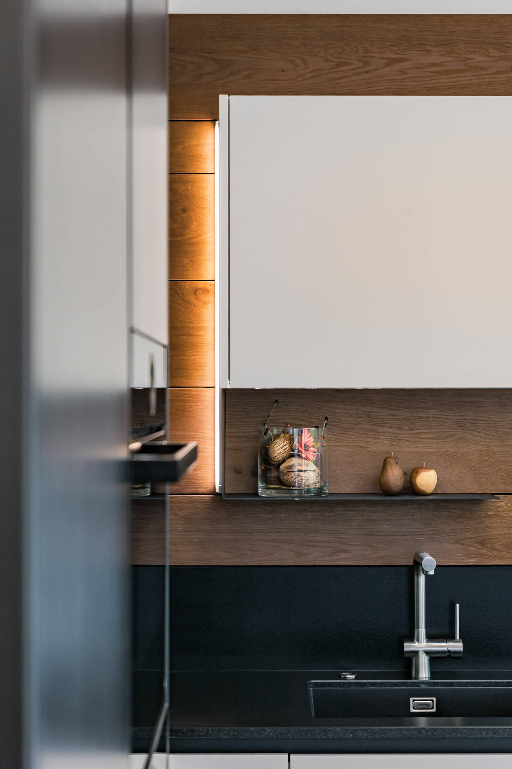 Moderne Küche mit Holzverkleidung, integrierter Beleuchtung und Edelstahlarmatur.