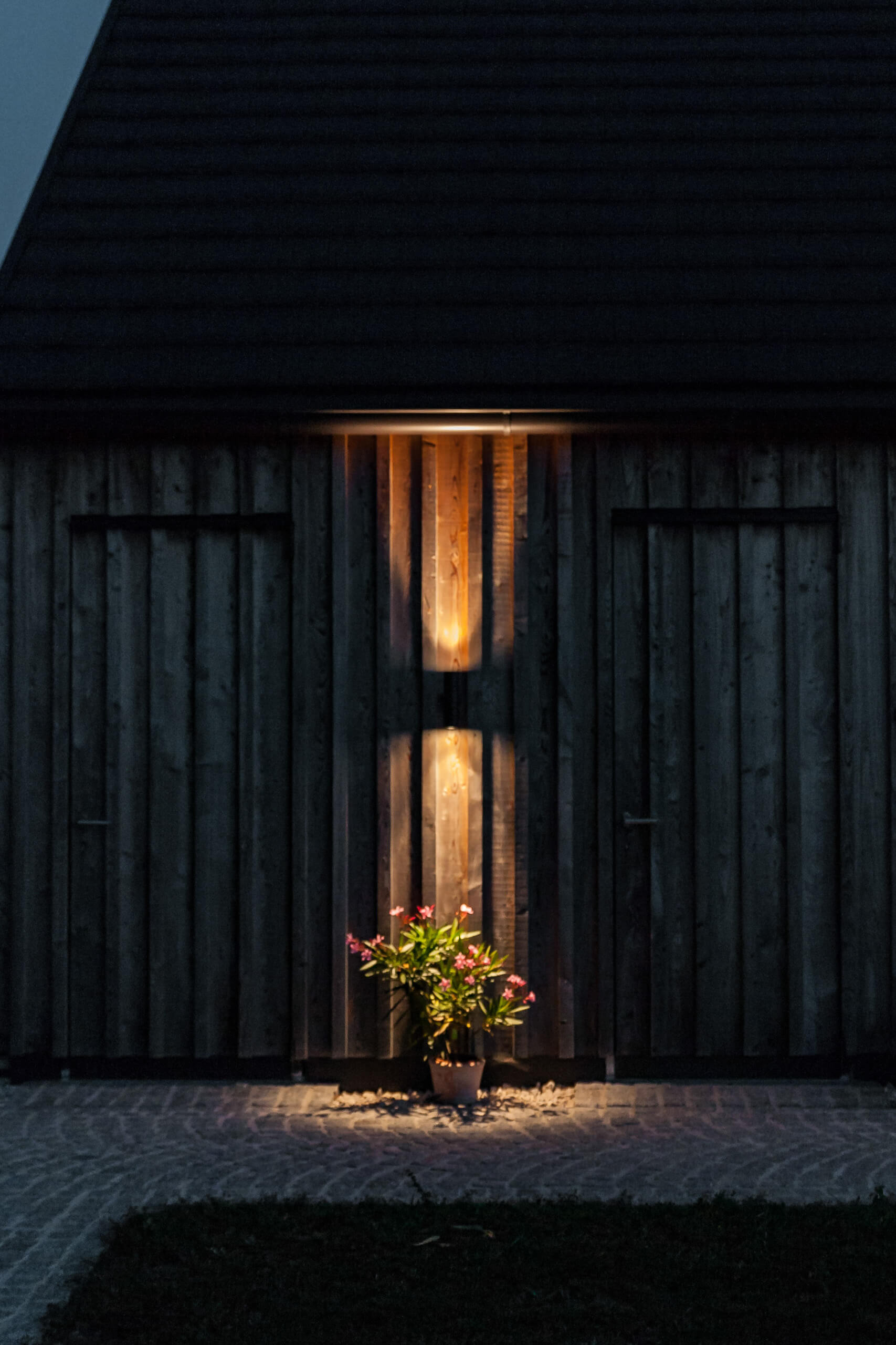 Holzfassade mit beleuchtetem Blumenkübel und Lichtreflexionen