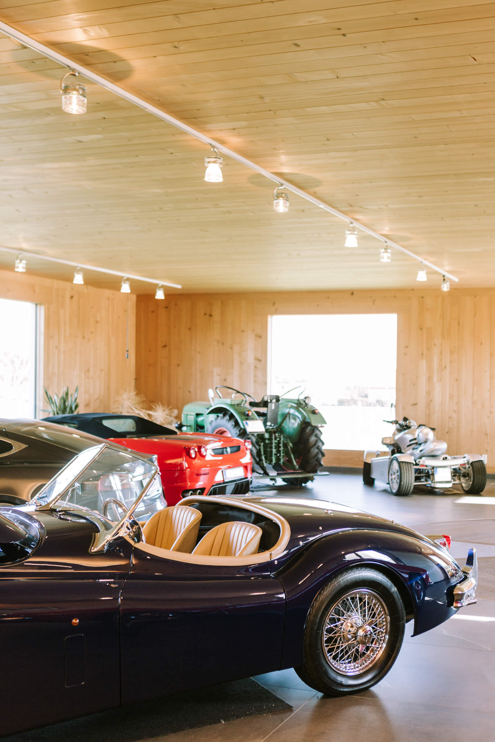 Edler Oldtimer-Sportwagen in dunklem Blau mit beiger Lederausstattung in einer hellen, holzgetäfelten Halle.