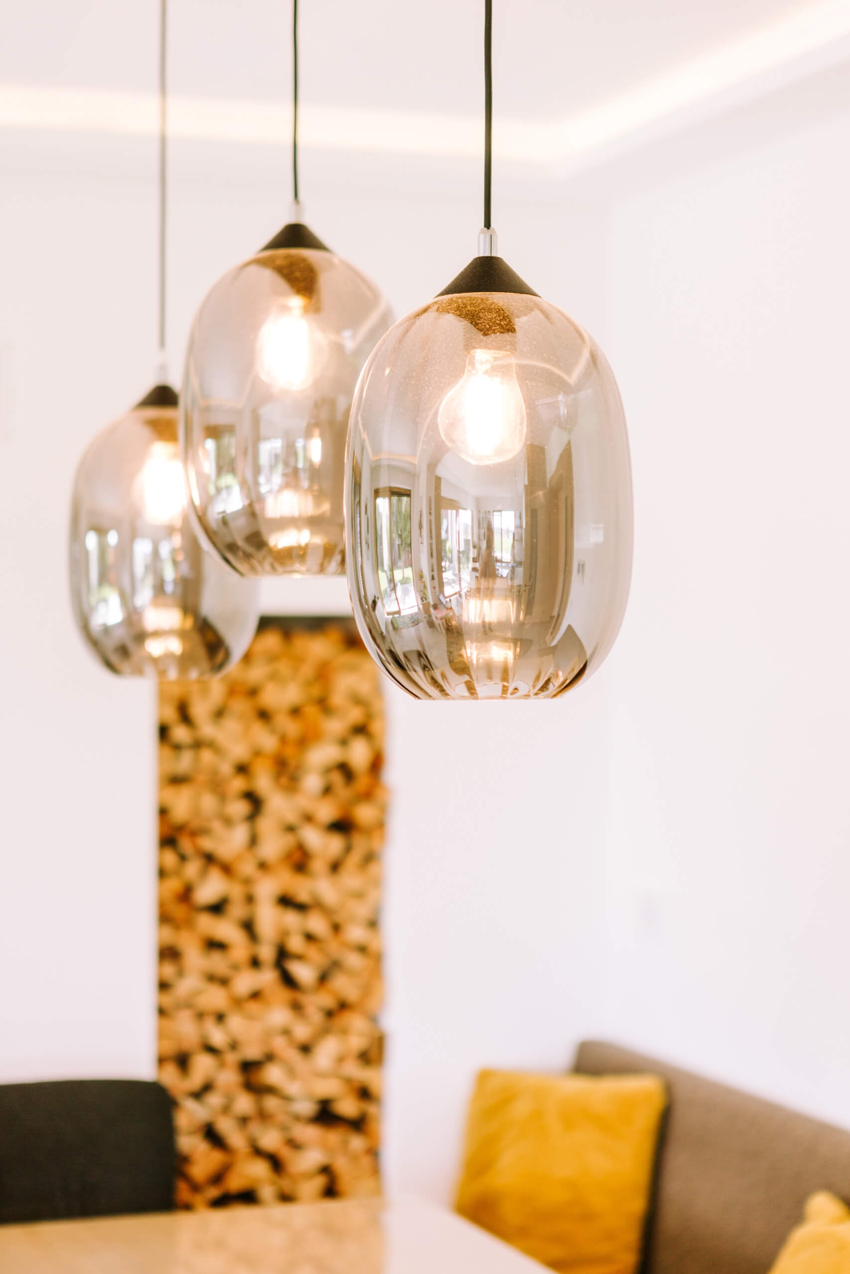 Hängende Glaspendelleuchten über einem Holzkamin und einem Tisch – Illumina Lichtplanung.