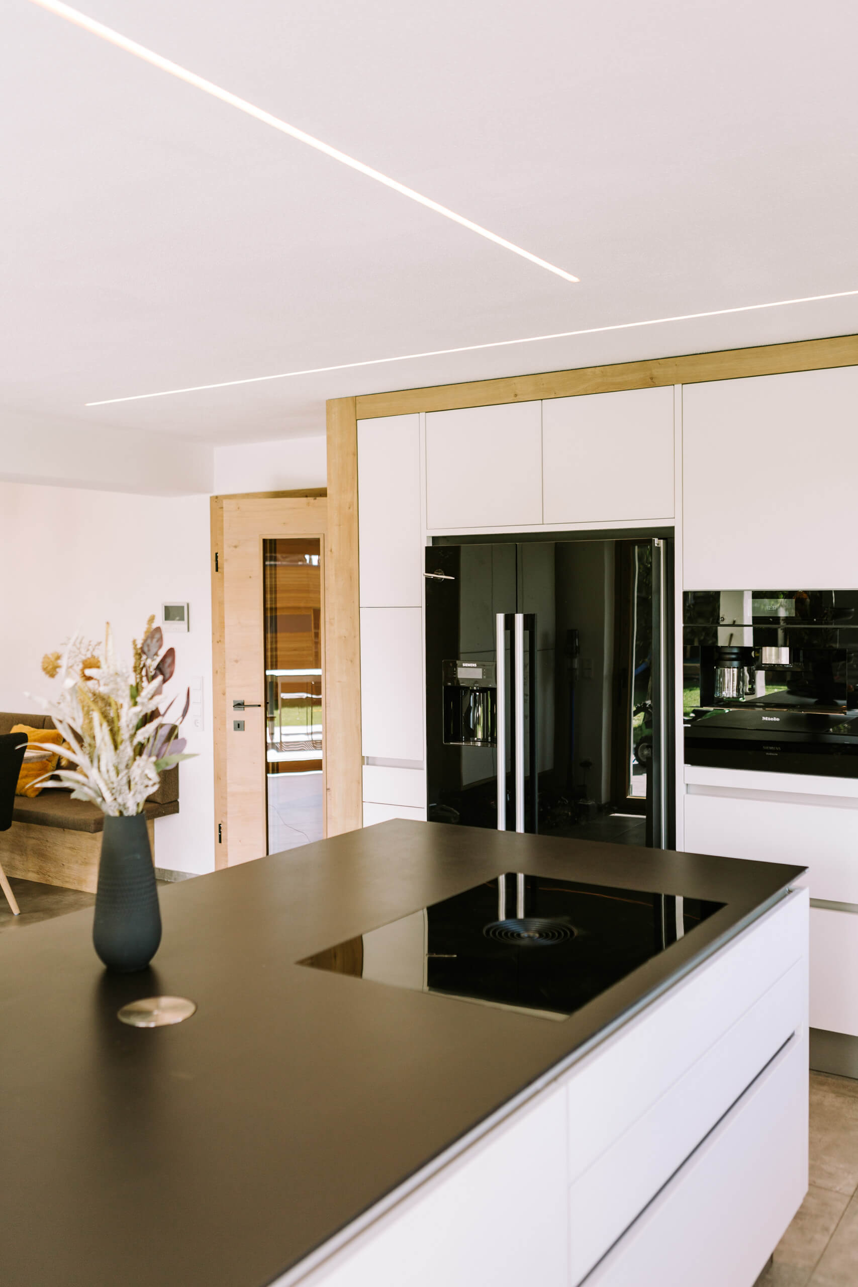 Moderne schwarze Kücheninsel mit Kochfeld und integriertem Lichtband an der Decke.