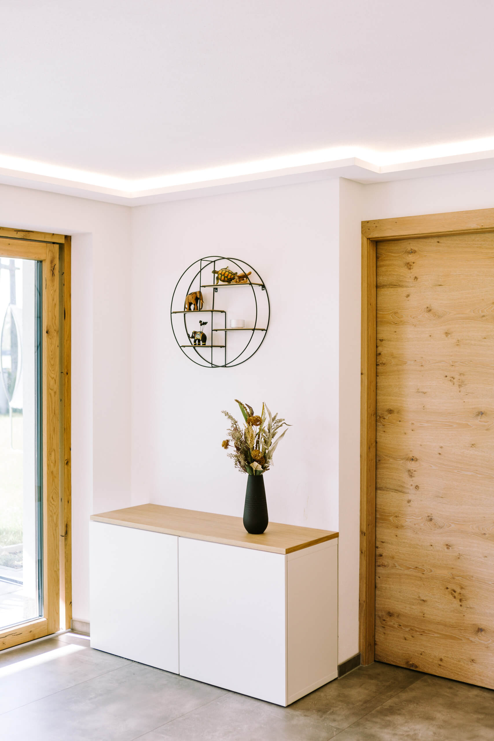 Moderne Diele mit weißem Sideboard, Holztür und indirekter Beleuchtung