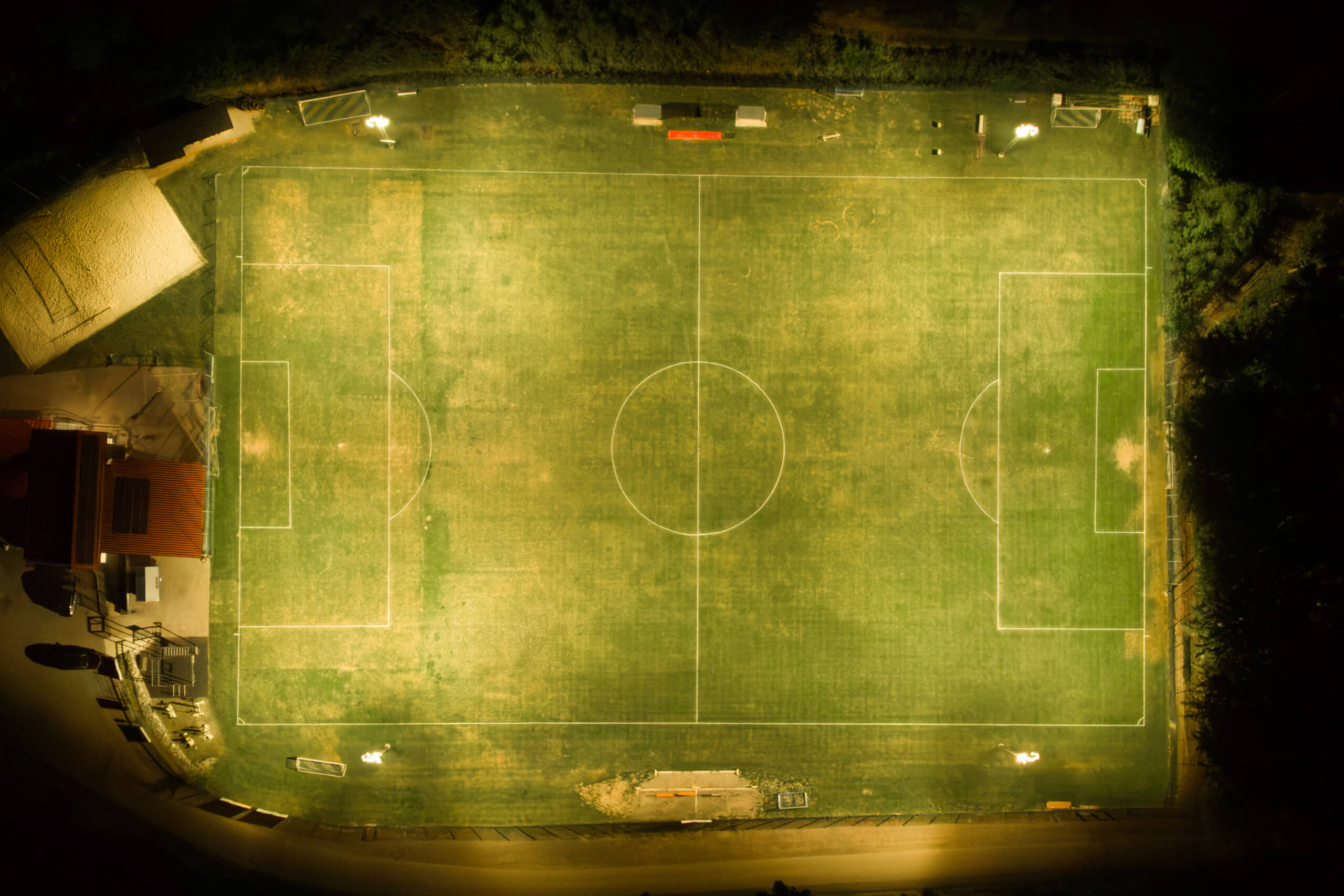 Beleuchtetes Fußballfeld bei Nacht mit Spielfeldmarkierungen und Flutlichtstrahlern
