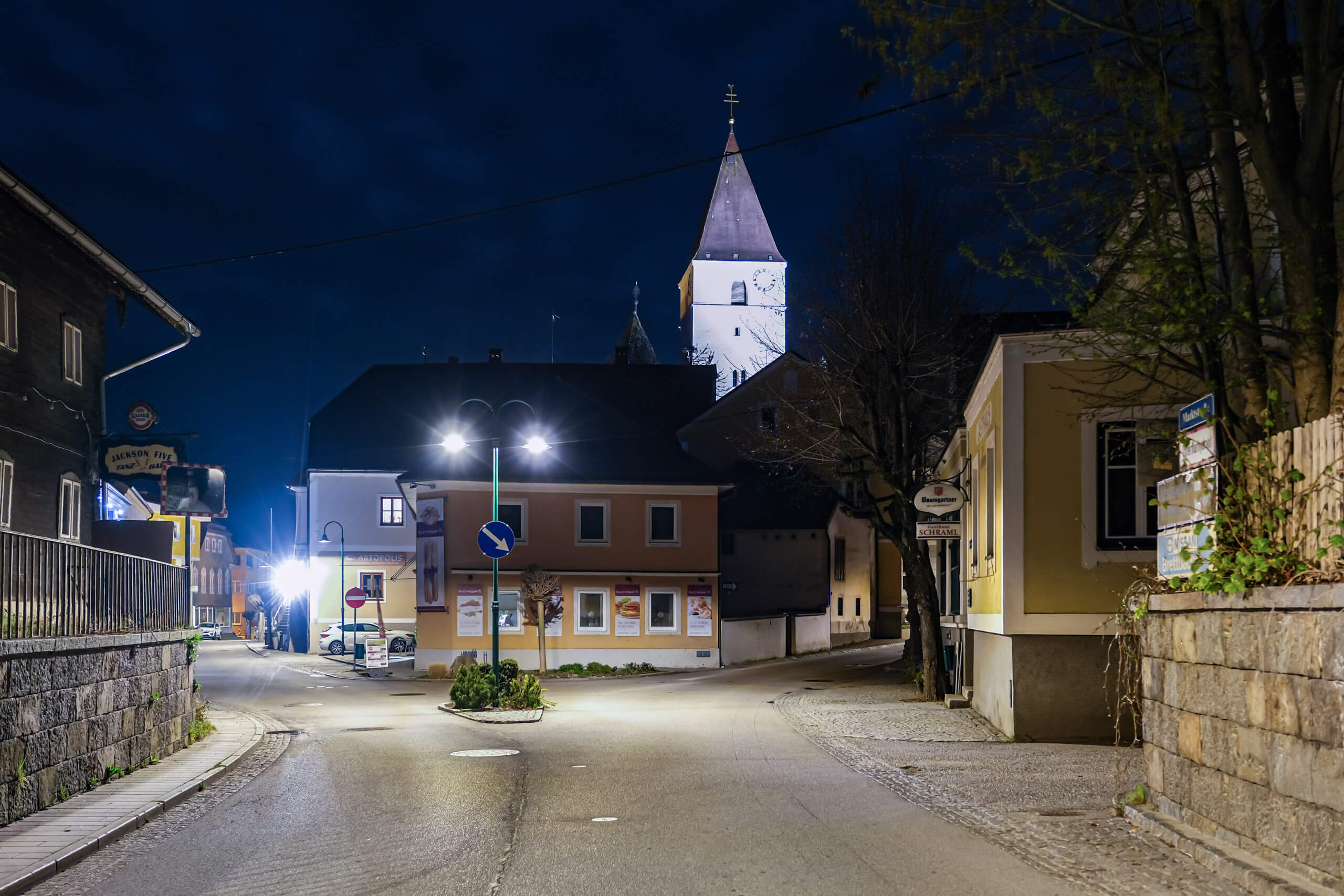Straßenbeleuchtung in einer kleinen Stadt bei Nacht, mit Kirche im Hintergrund.