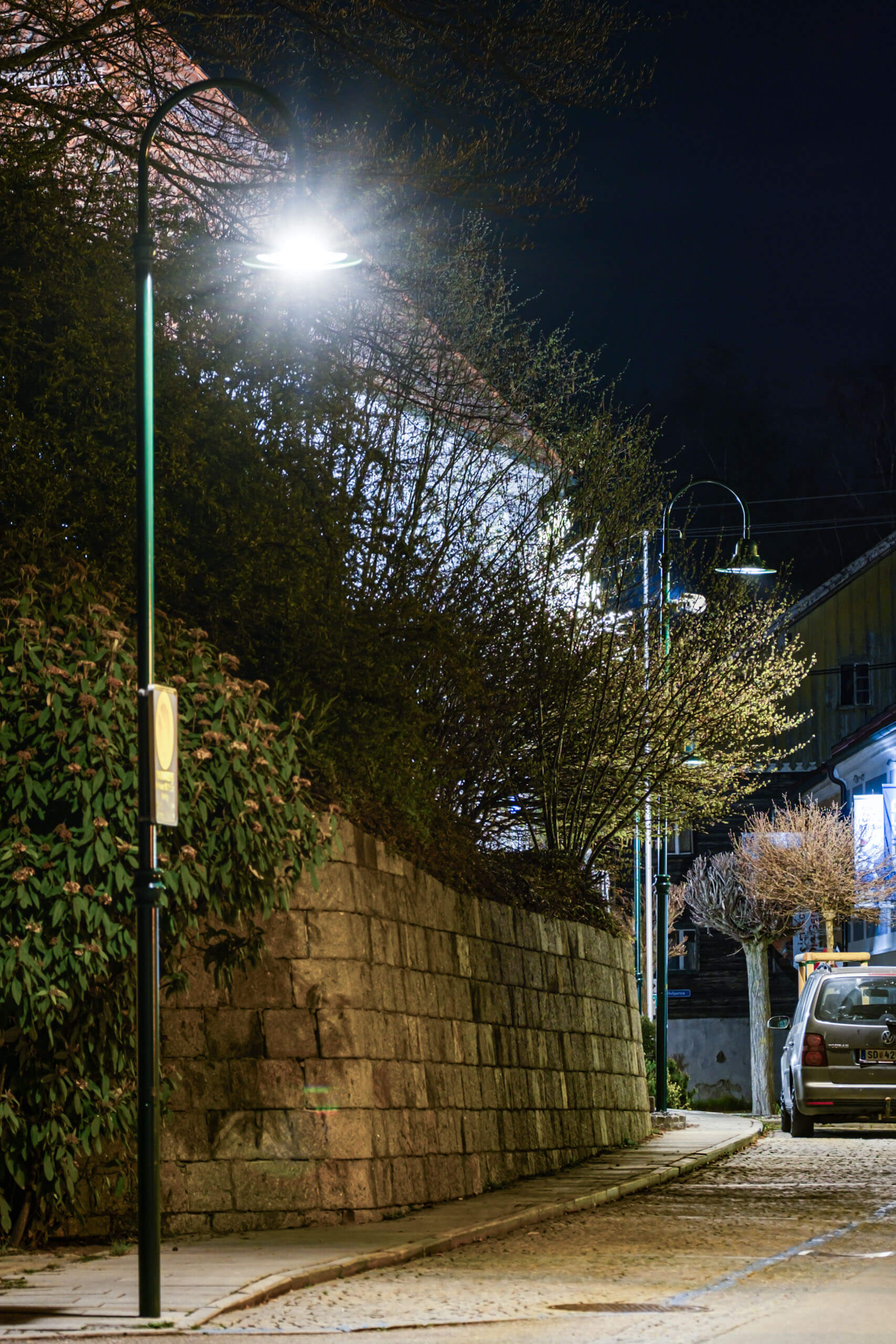 Beleuchtete Straße mit Steinmauer und Bäumen bei Nacht